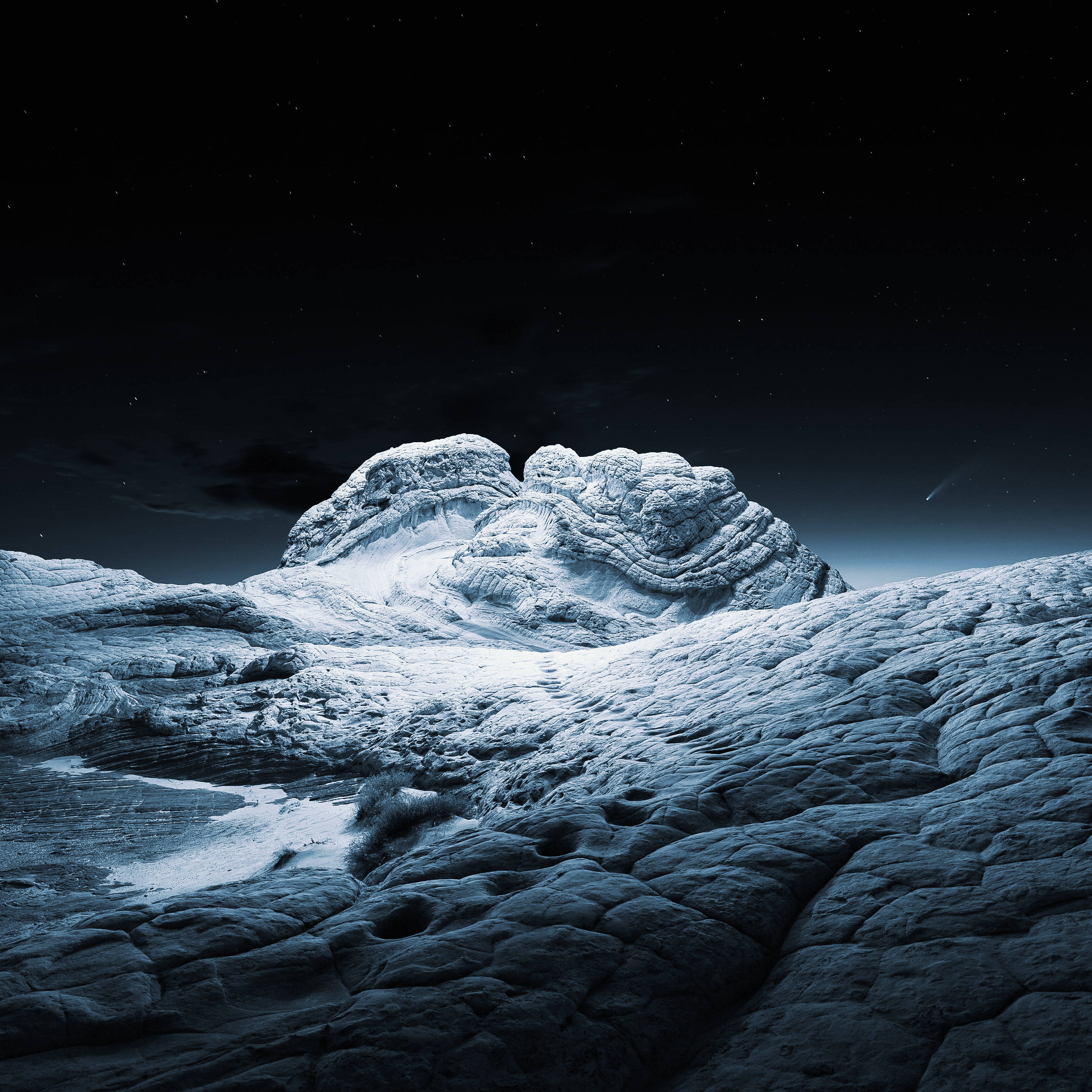 macOS Big Sur 幻境岩石 壁紙 — 在繁星點點的夜空下，一座積雪的山峰，一顆微弱的彗星劃過黑暗的天空。