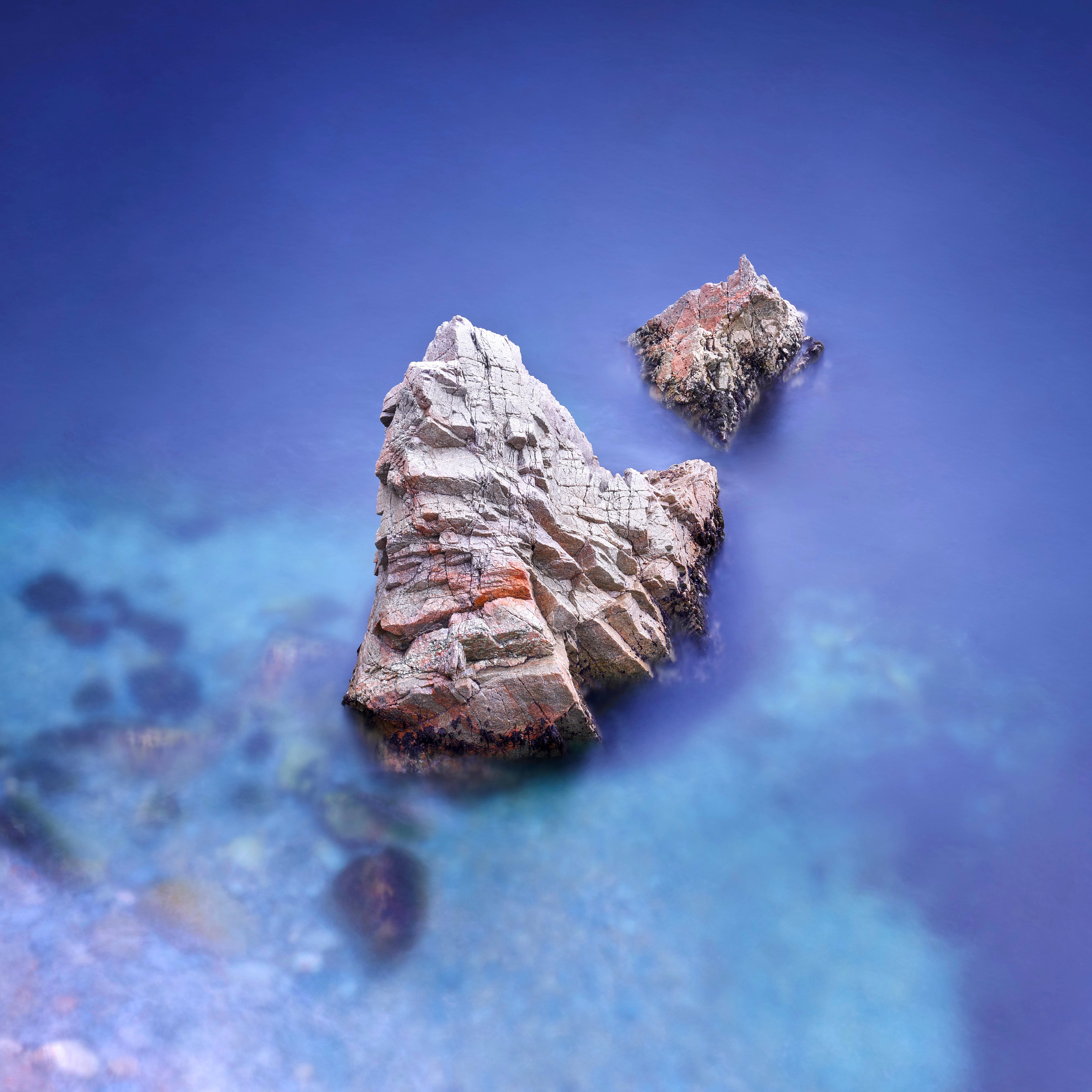 macOS Big Sur 水面 壁紙 — 兩個崎嶇的海蝕柱從碧綠色的海水中升起，在深藍色的天空下，波浪因運動而模糊。
