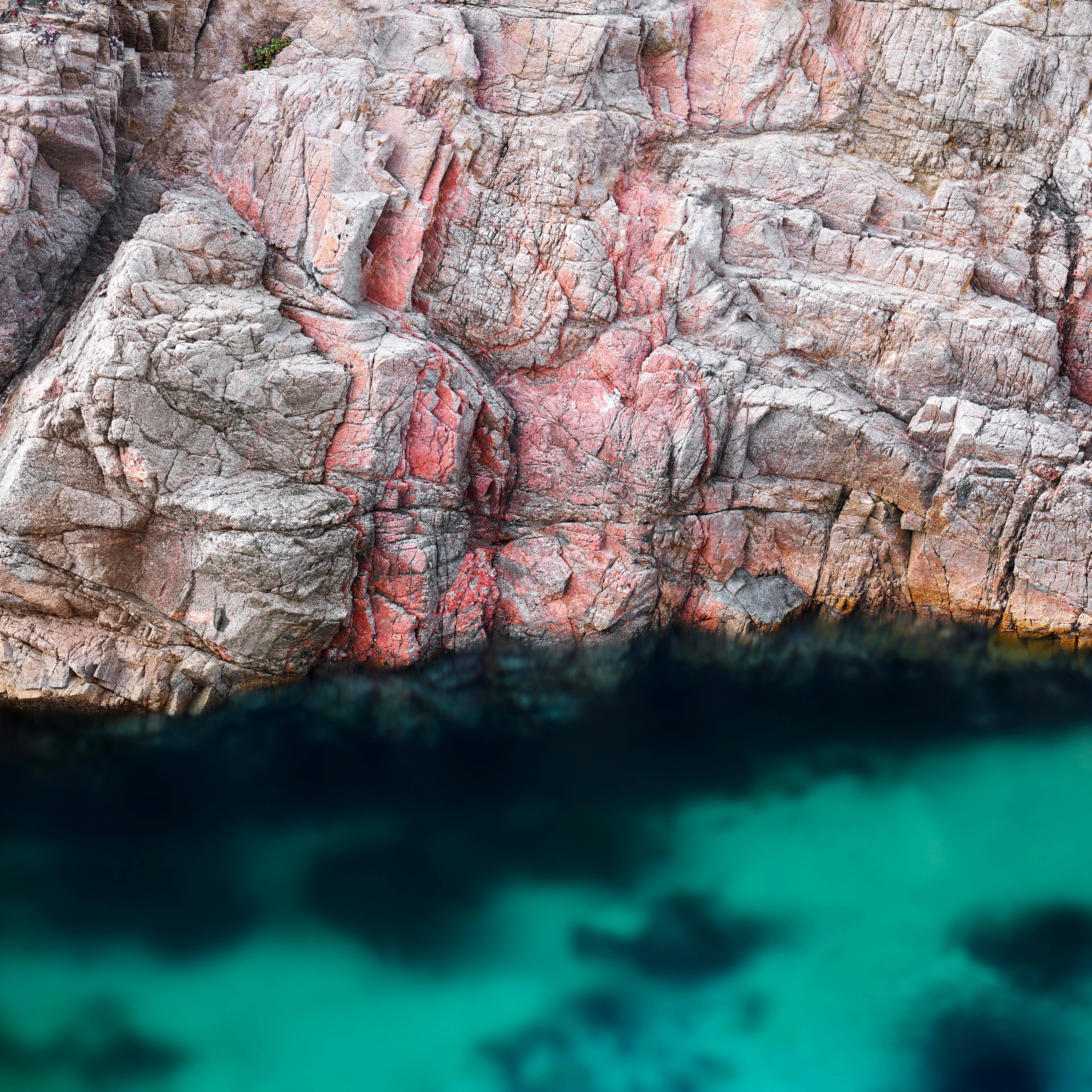 macOS Big Sur 深水 壁紙 — 崎嶇的粉紅色和灰色懸崖聳立在清澈的碧綠海水之上，呈現寧靜的海岸景色。
