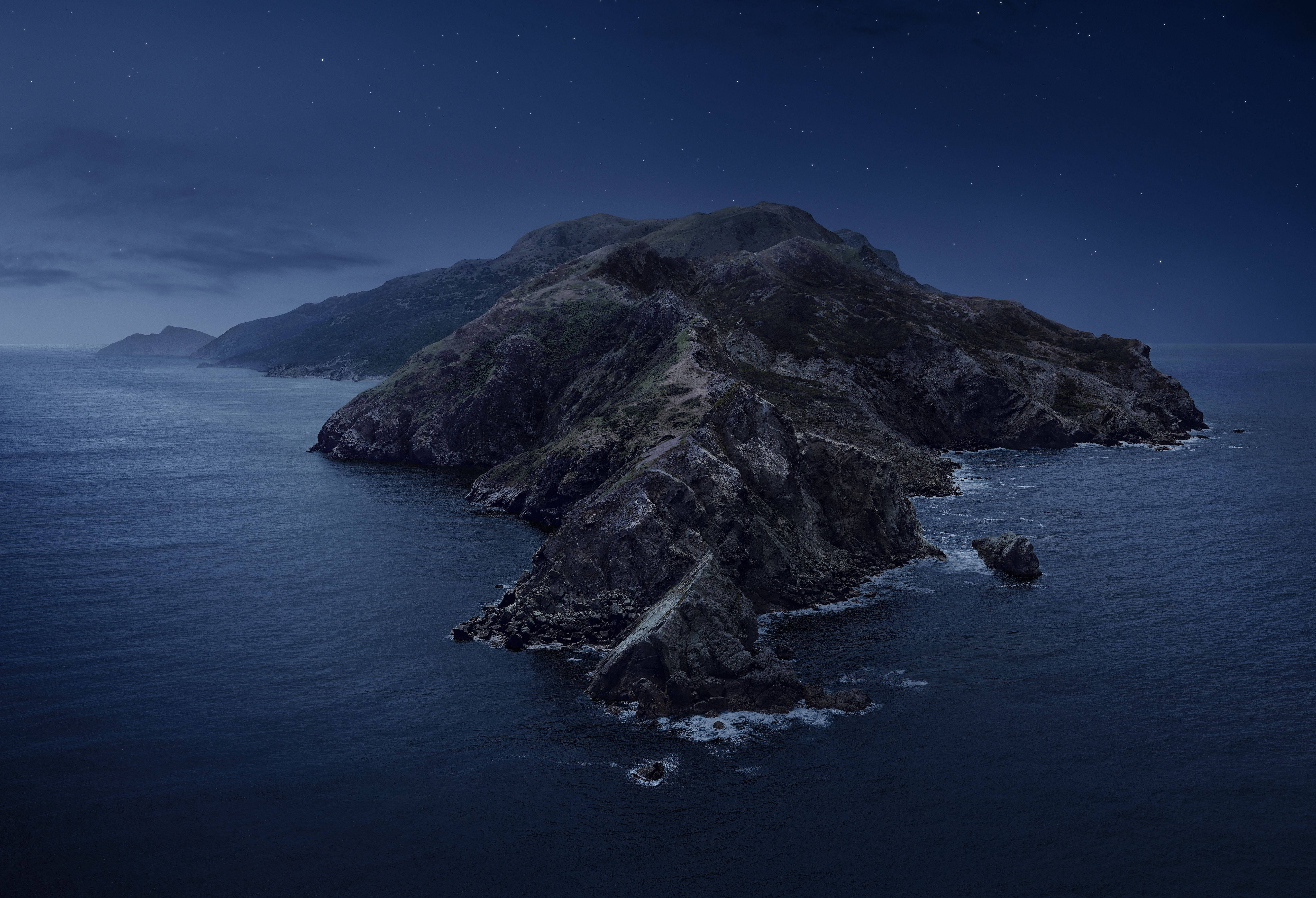 macOS Catalina 夜景 壁紙 — 一座崎嶇的岩石島嶼從深藍色的海洋中升起，在繁星點點的夜空下，溫柔的海浪拍打著懸崖。