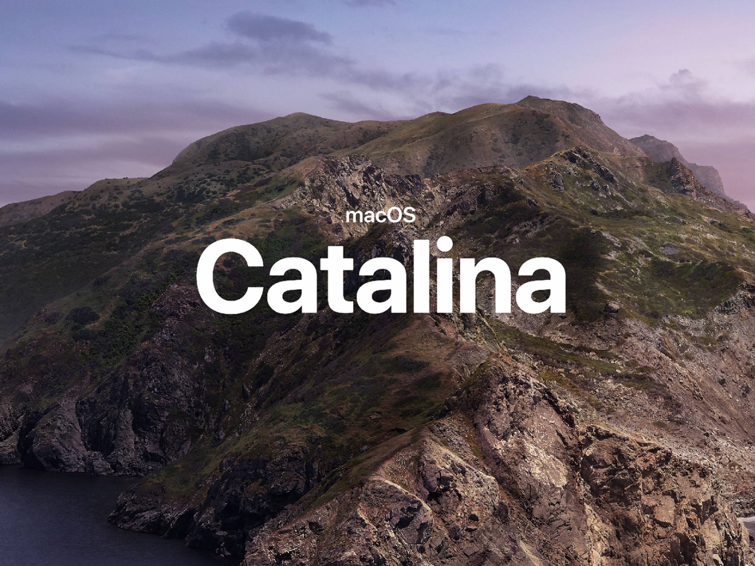 macOS Catalina 特寫 壁紙 — 黃昏時分崎嶇的山區海岸線，帶有柔和的紫色和藍色天空，並覆蓋了 macOS Catalina 文字。