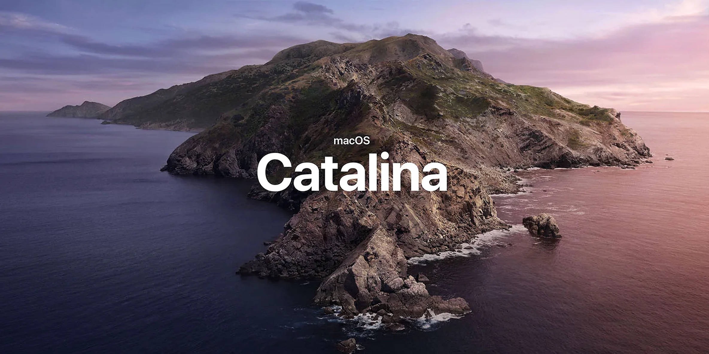 macOS Catalina 第十六版 壁紙 — 一個崎嶇的島嶼，有岩石峭壁和綠色斜坡，從深藍色的海水中升起，在柔和的粉紅色和紫色暮色天空下。