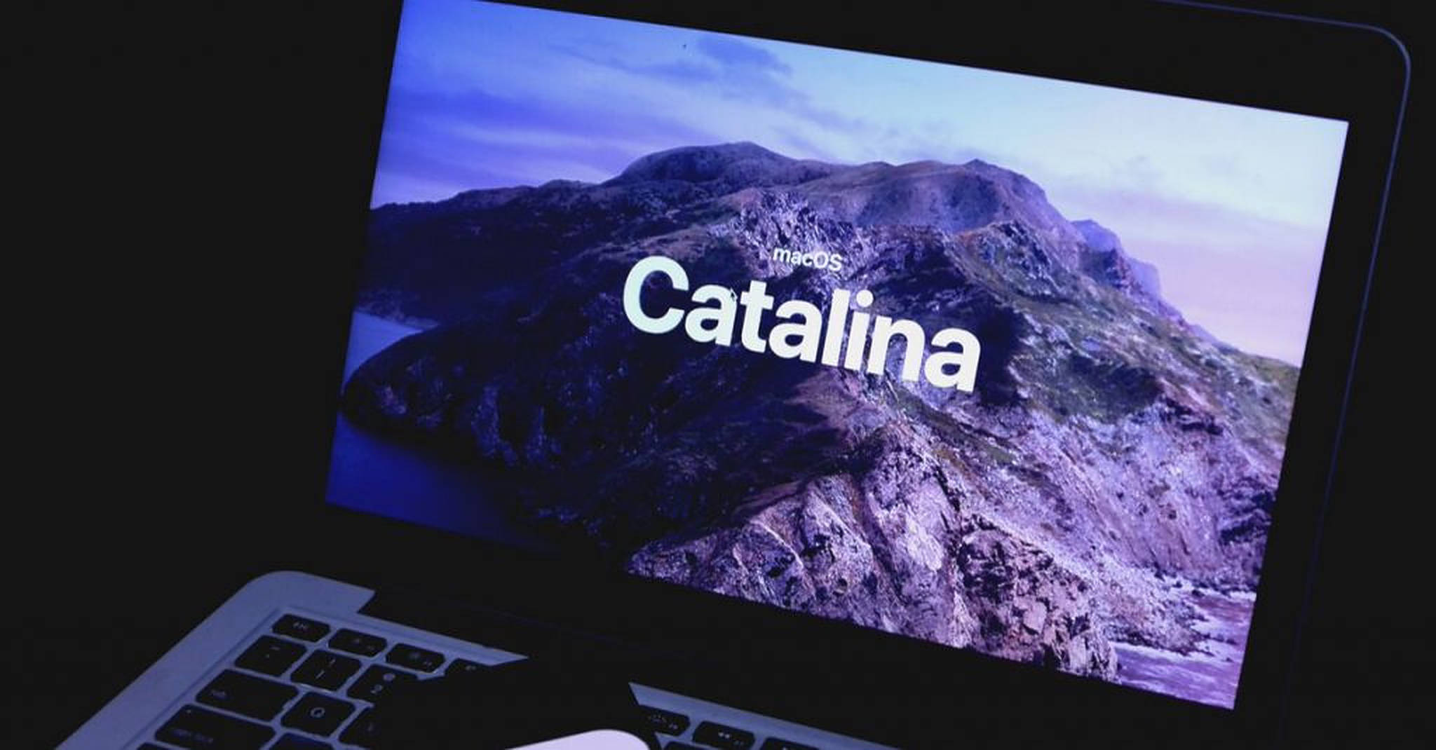 macOS Catalina 筆記本電腦螢幕 壁紙 — 一部筆記型電腦顯示macOS Catalina的啟動畫面，背景是暮色天空下的紫色山脈景觀。