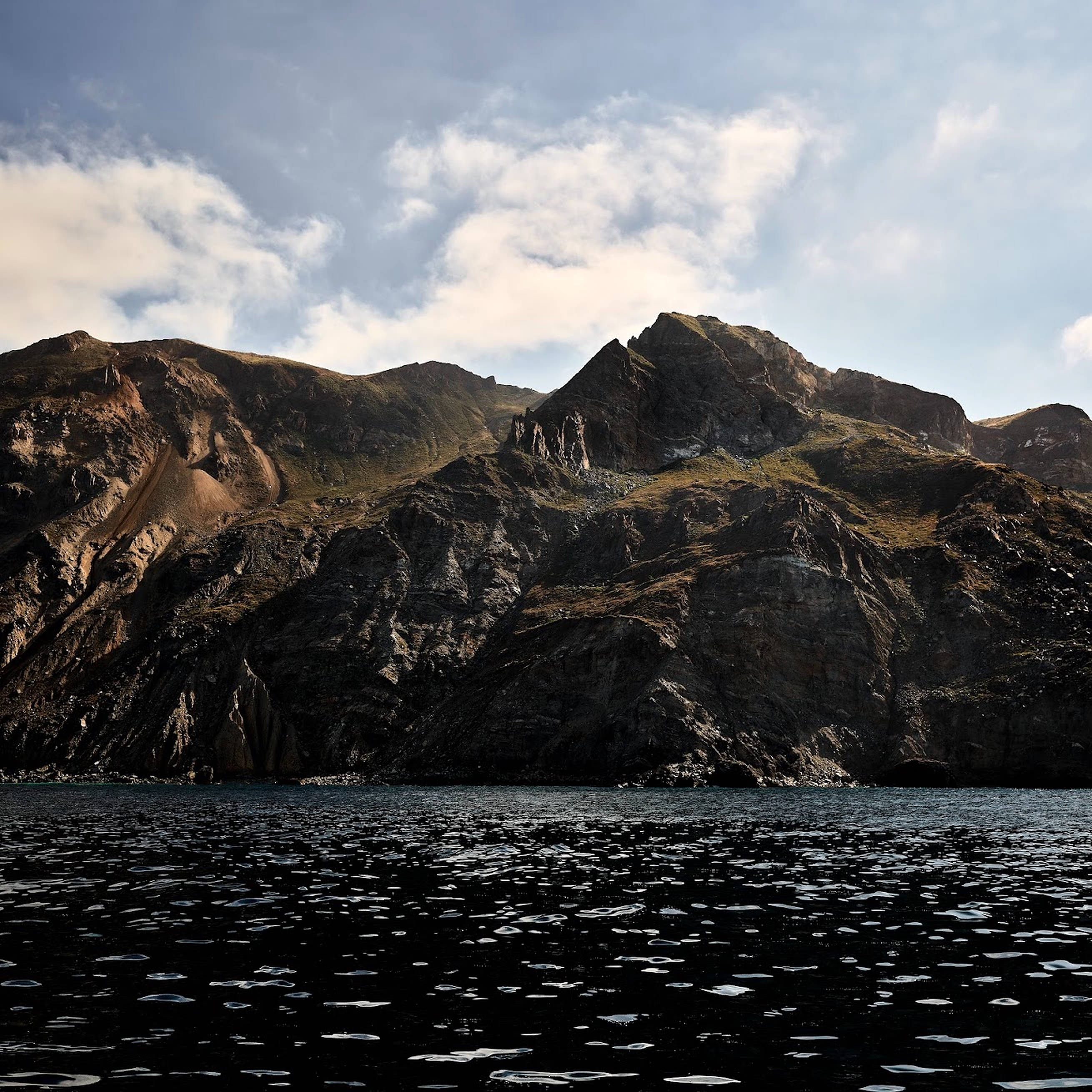 macOS Catalina 黑海 壁紙 — 崎嶇的山峰聳立於深色水面上，水面散落著浮冰，天空局部多雲。