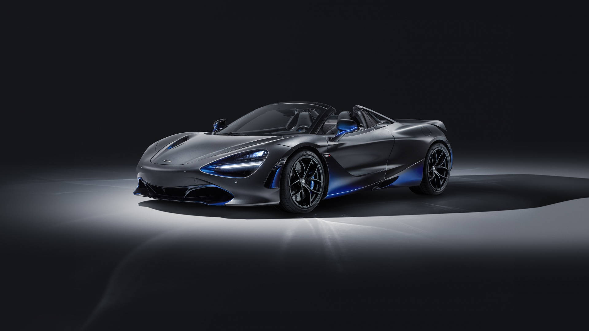 在黑暗的攝影棚環境中，一輛帶有藍色燈光點綴的啞光灰色McLaren 720S Spider。