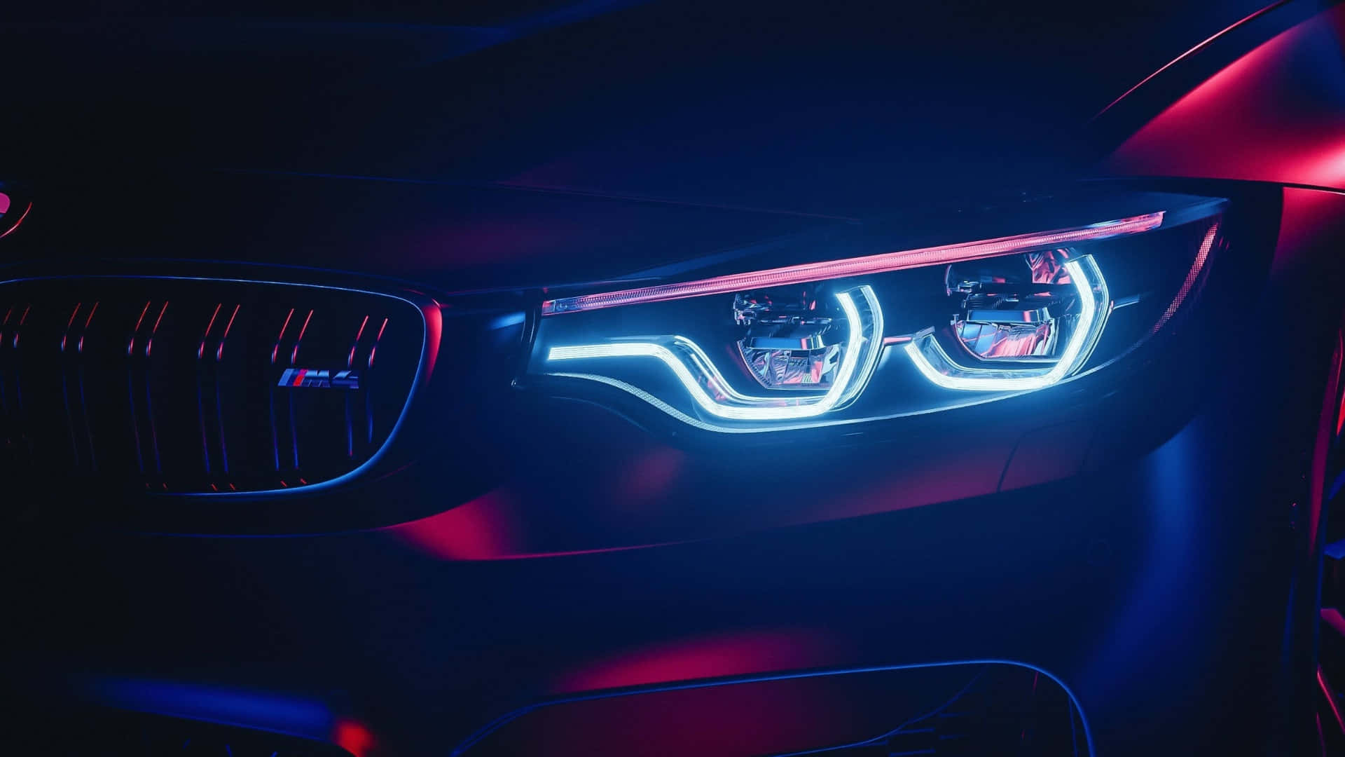 macOS Tahoe 深色模式 壁紙 — BMW M4 發光藍色和紅色頭燈在黑暗工作室中帶有霓虹反射的特寫。