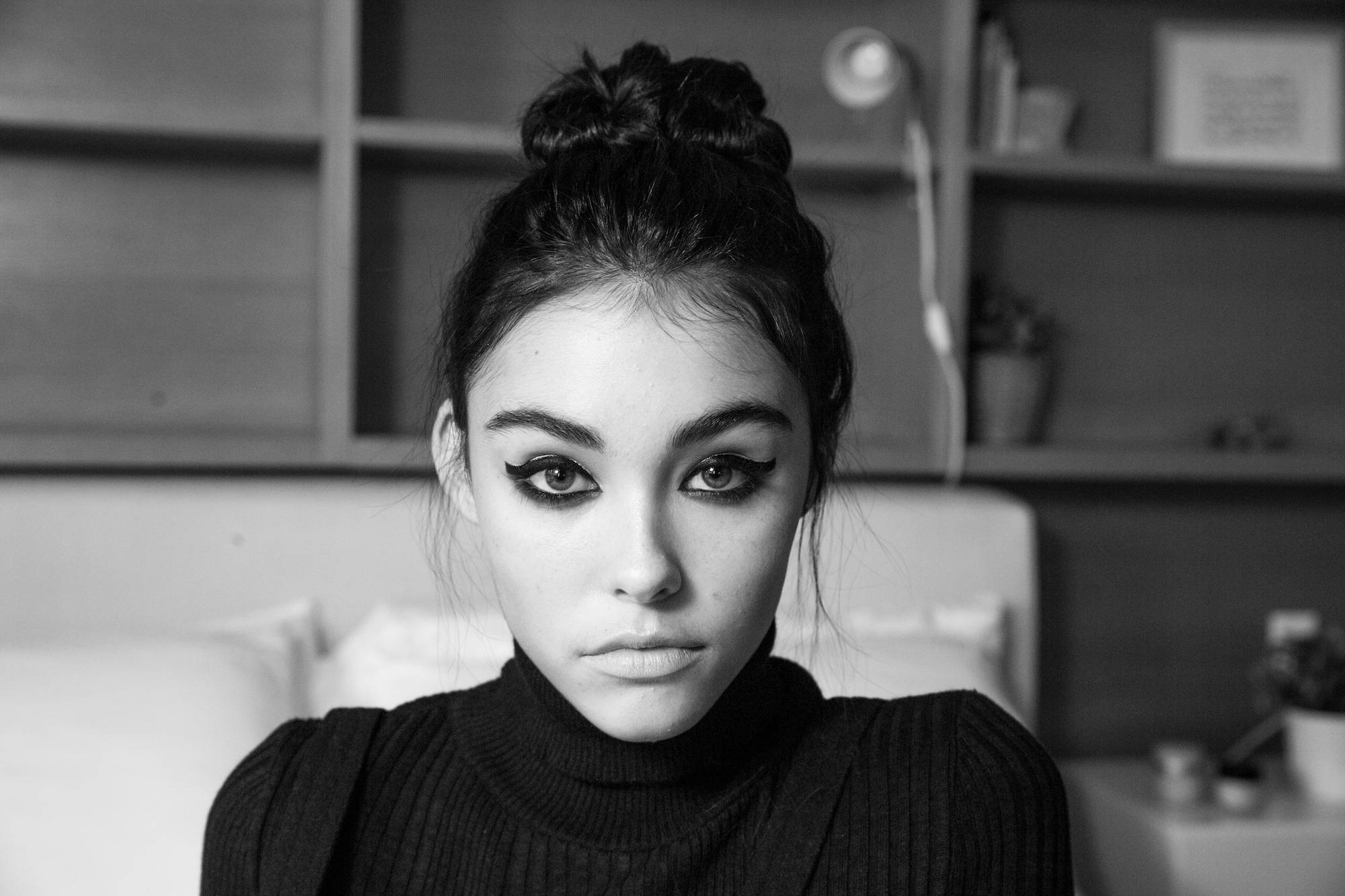 Madison Beer 單色寫真 壁紙 — 一個黑白肖像，一位年輕女性帶著戲劇性的眼線和髮髻，在臥室裡直視鏡頭。