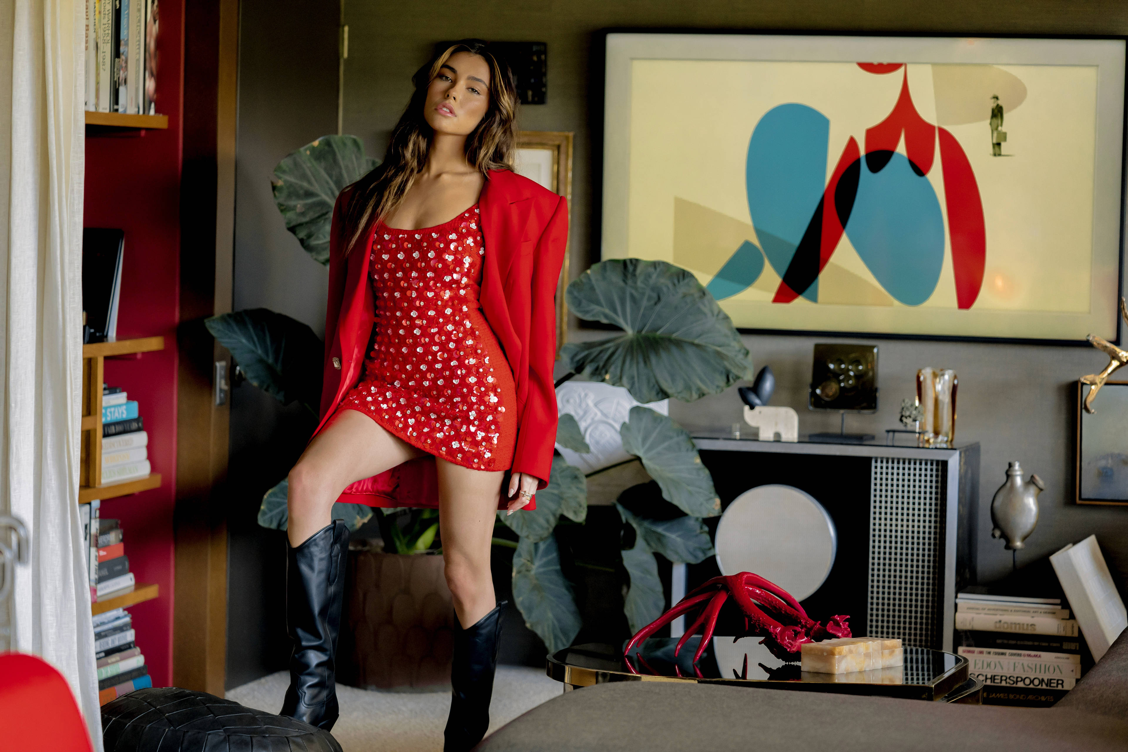 Madison Beer 秋季 Remix 封面 壁紙 — 一位身穿紅色亮片連衣裙和配套西裝外套的女性在時尚裝飾的現代客廳中自信地擺姿勢。