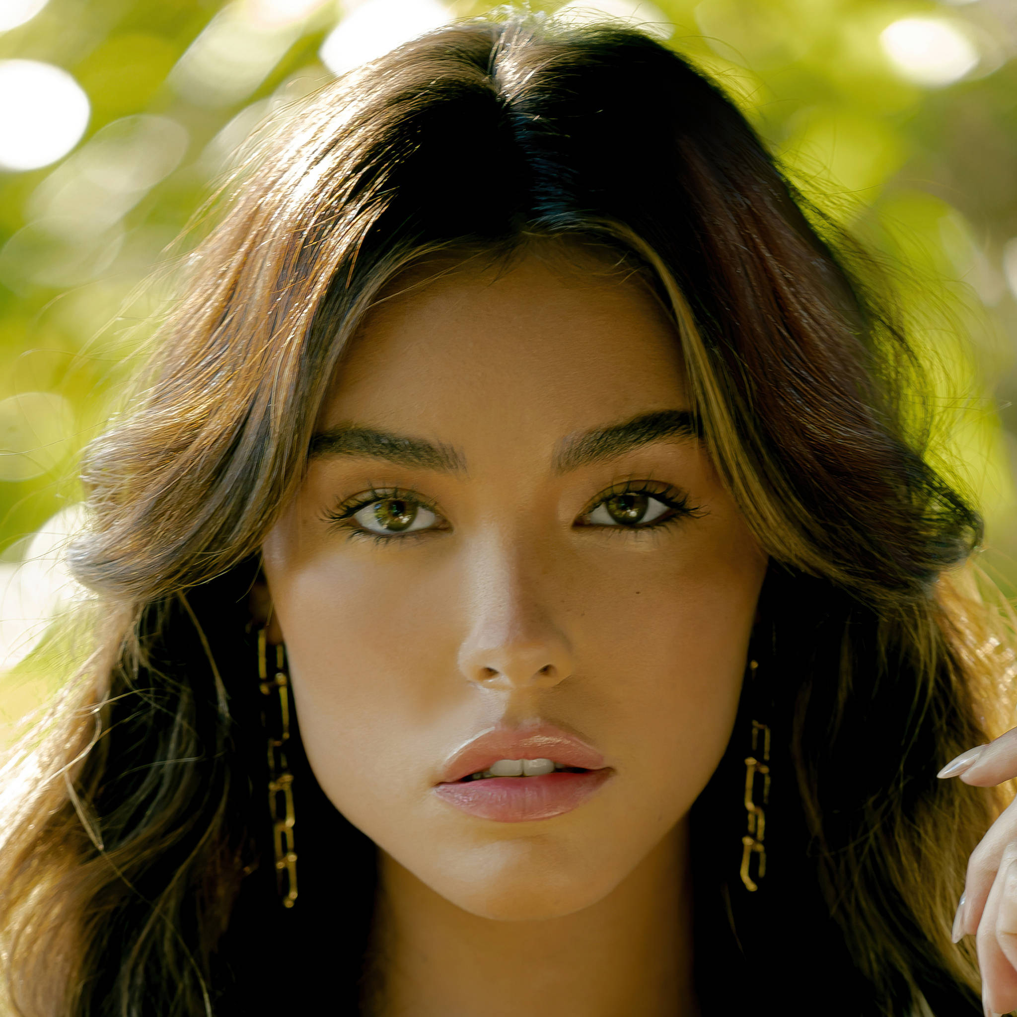 Madison Beer 近照 Remix 雜誌封面 壁紙 — 一個近距離肖像，一名擁有波浪棕色頭髮和金色鏈條耳環的女性，在明亮的綠色散景背景下直視鏡頭。