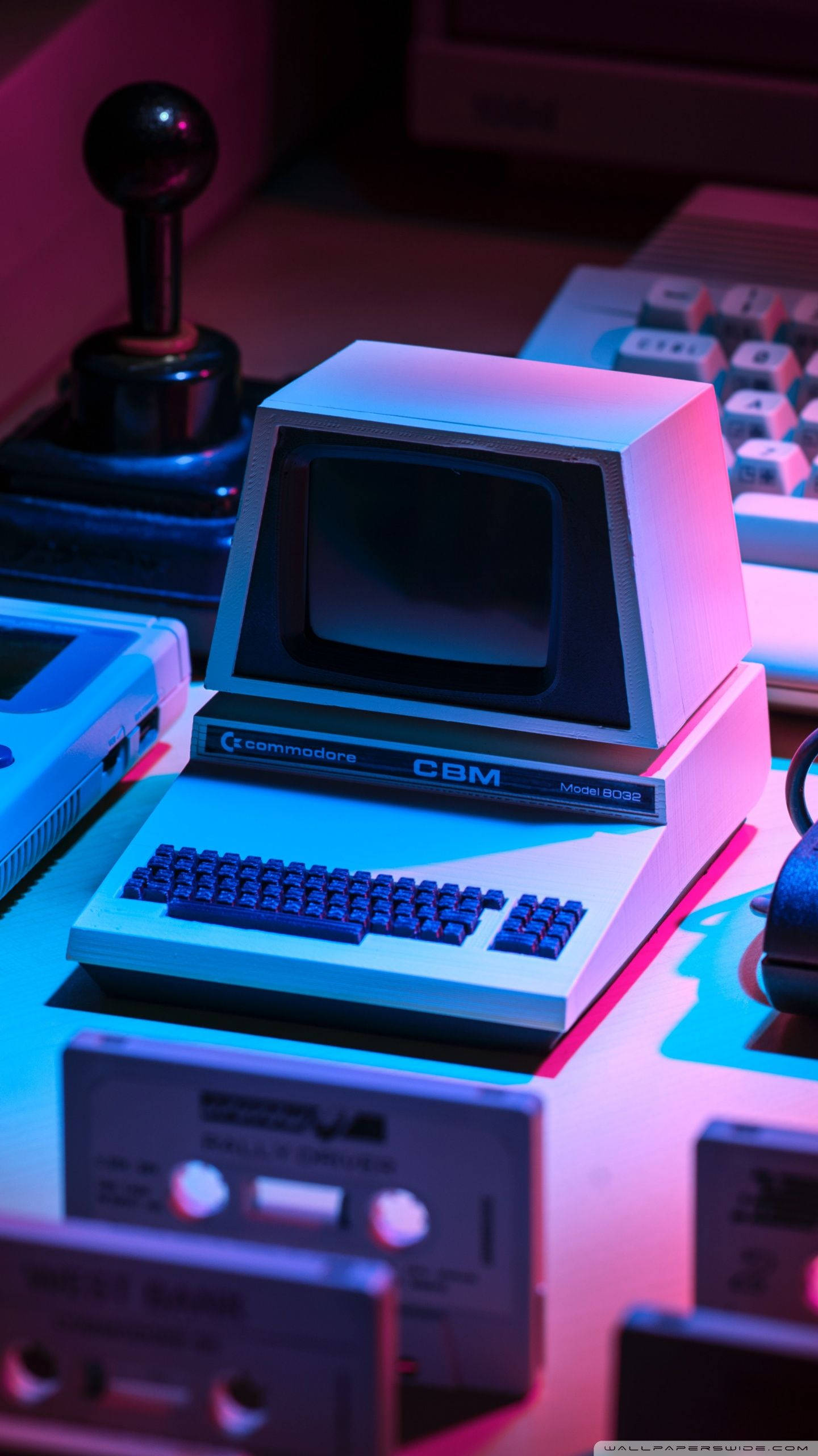 Magnavox Odyssey復古鍵盤 壁紙 — 一部浸沒在霓虹粉紅和藍光中的復古 Commodore CBM 電腦，周圍環繞著復古遊戲裝備。