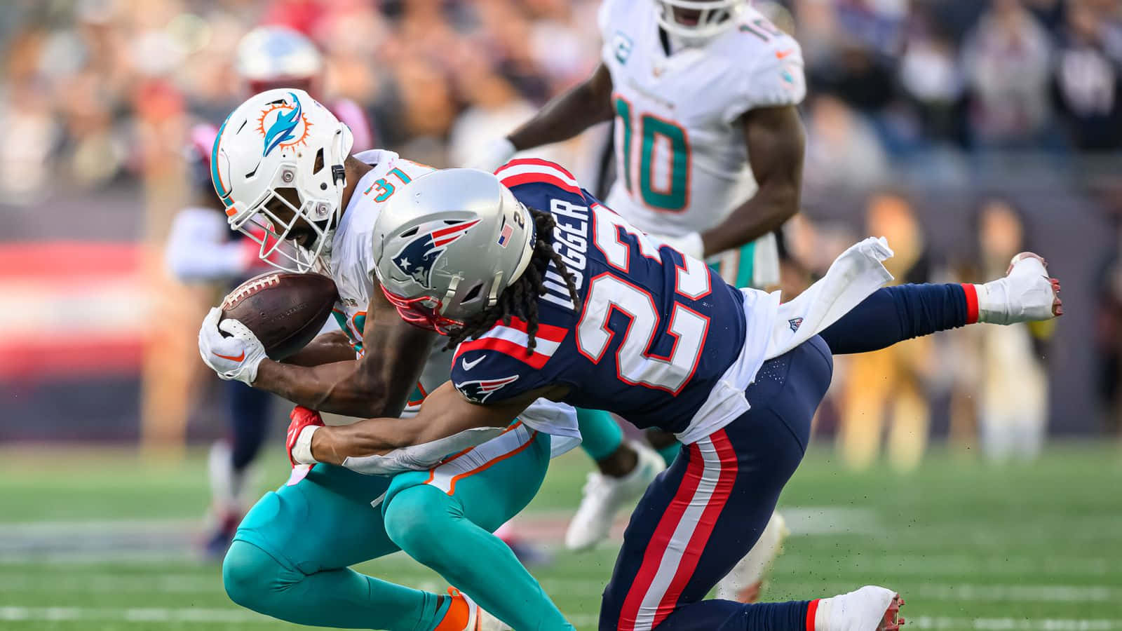  壁紙 — 邁阿密海豚隊的一名接球手在激烈的NFL美式足球比賽中被新英格蘭愛國者隊的防守球員擒抱。