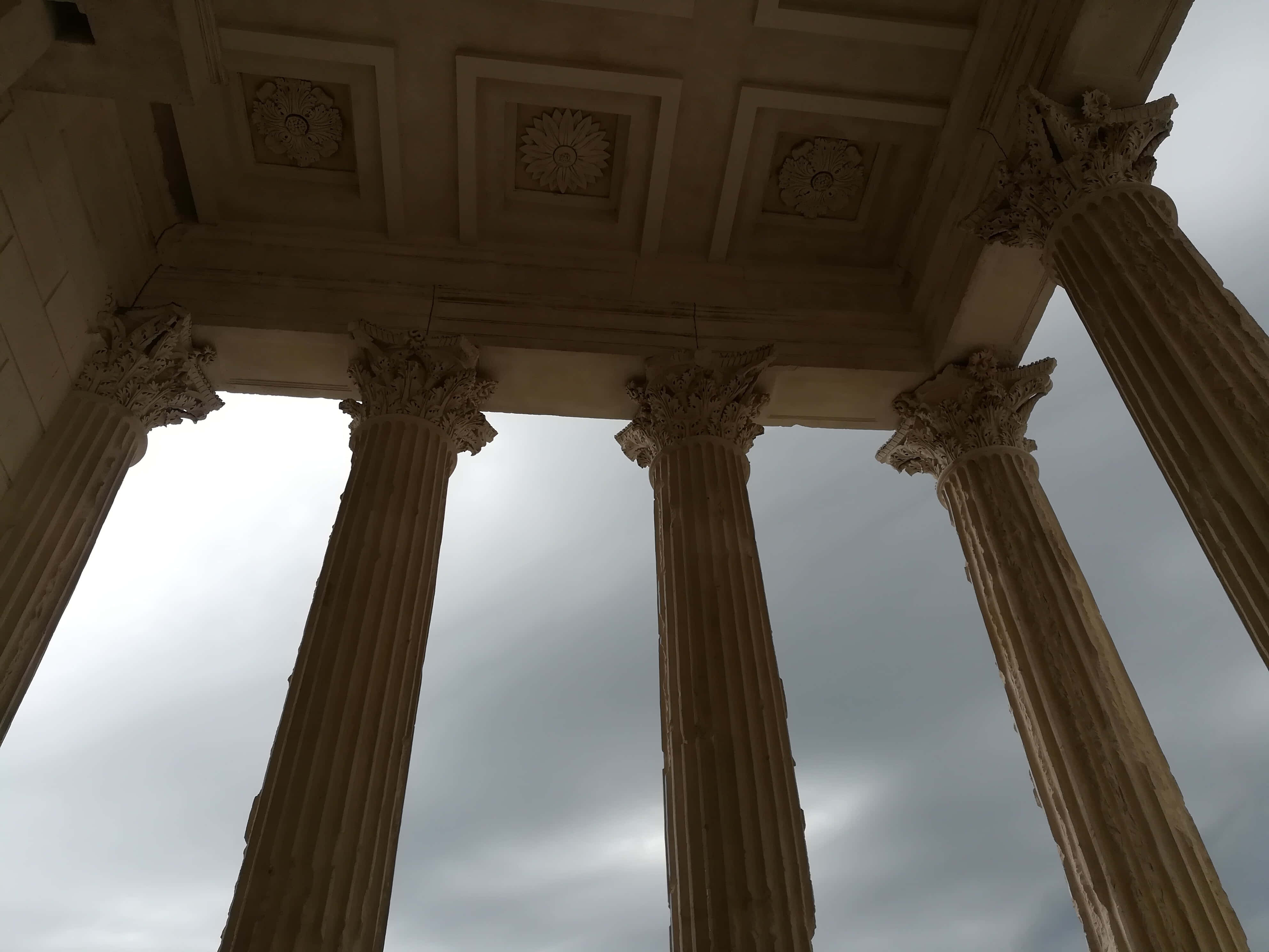 法國 Maison Carrée 柱廊陰鬱天色 壁紙 — 宏偉的古典柱子在戲劇性的低角度拍攝中，向陰沉的陰天升起。