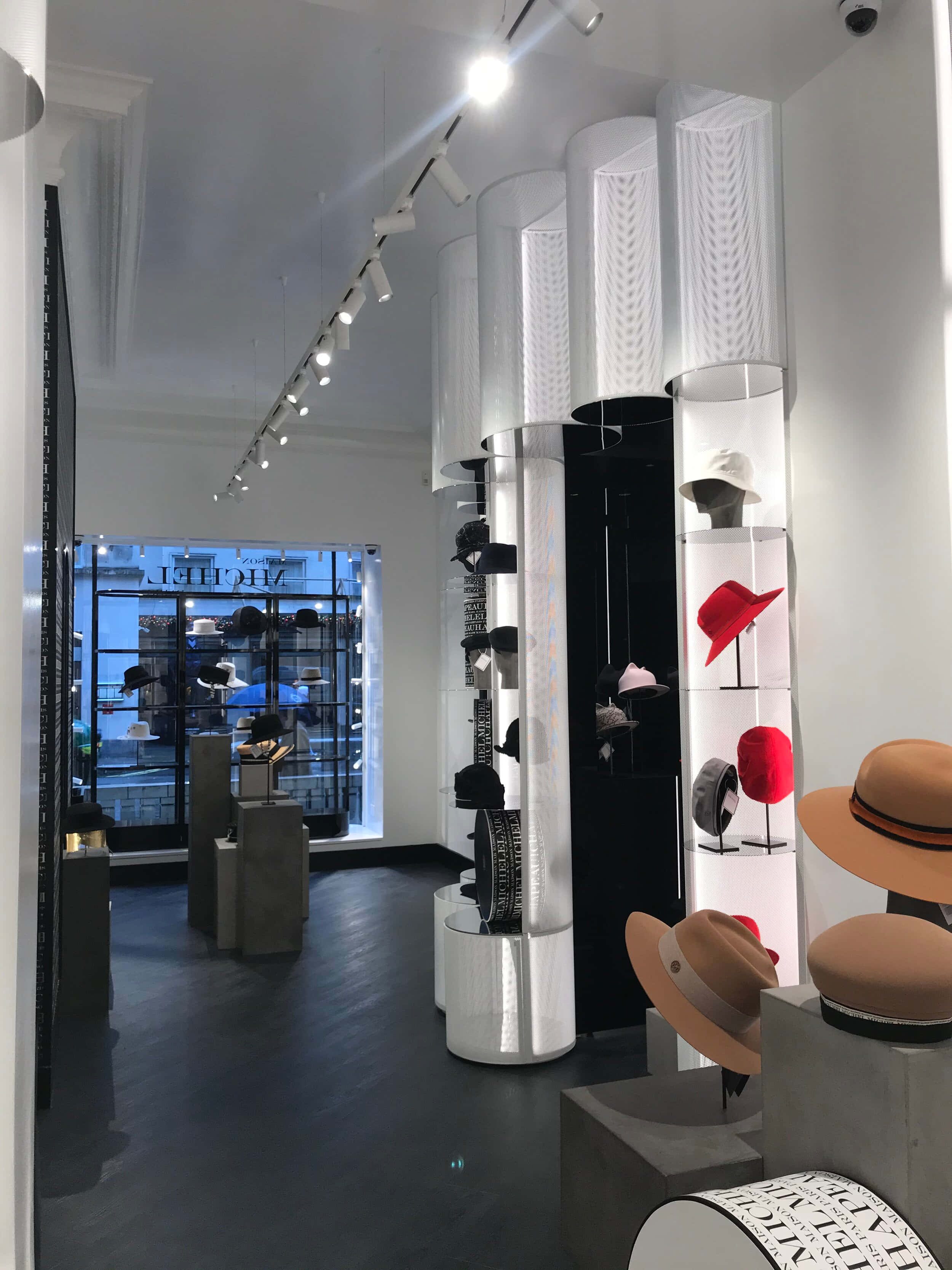 Maison Michel 店內 壁紙 — 現代帽子精品店，採用時尚白色柱子，在明亮的軌道燈光下展示色彩繽紛的帽子。