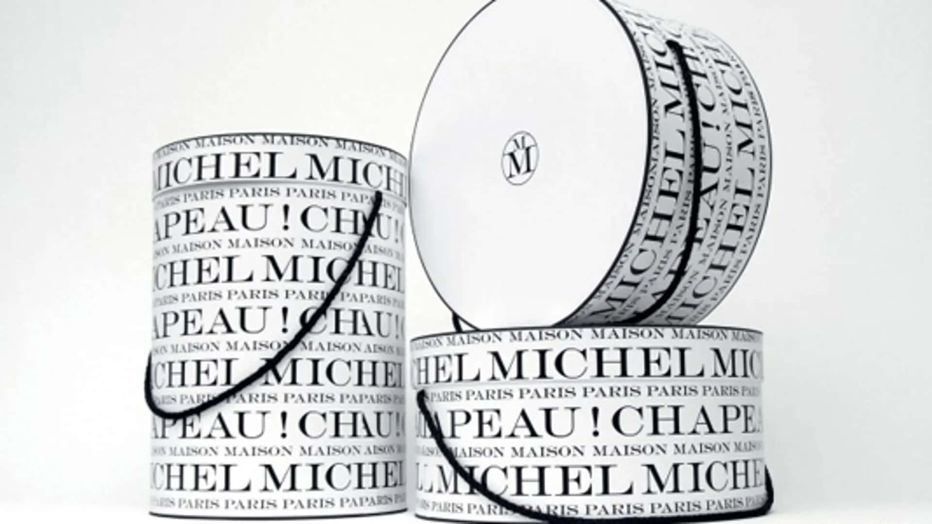 Maison Michel 帽盒系列 壁紙 — 三個極簡風格的圓柱形容器，帶有重複的黑色文字和標誌，背景為純白色。