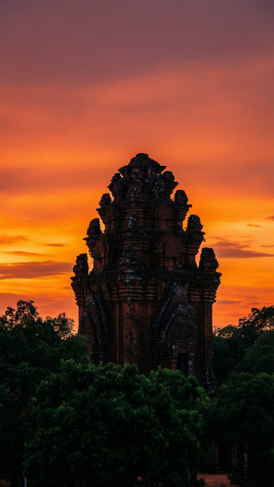 Temple Silhouette Sunset 壁紙 — 一座雄偉的古老石廟在熾熱的橙色和粉紅色日落天空的映襯下形成剪影，下方是鬱鬱蔥蔥的綠樹。