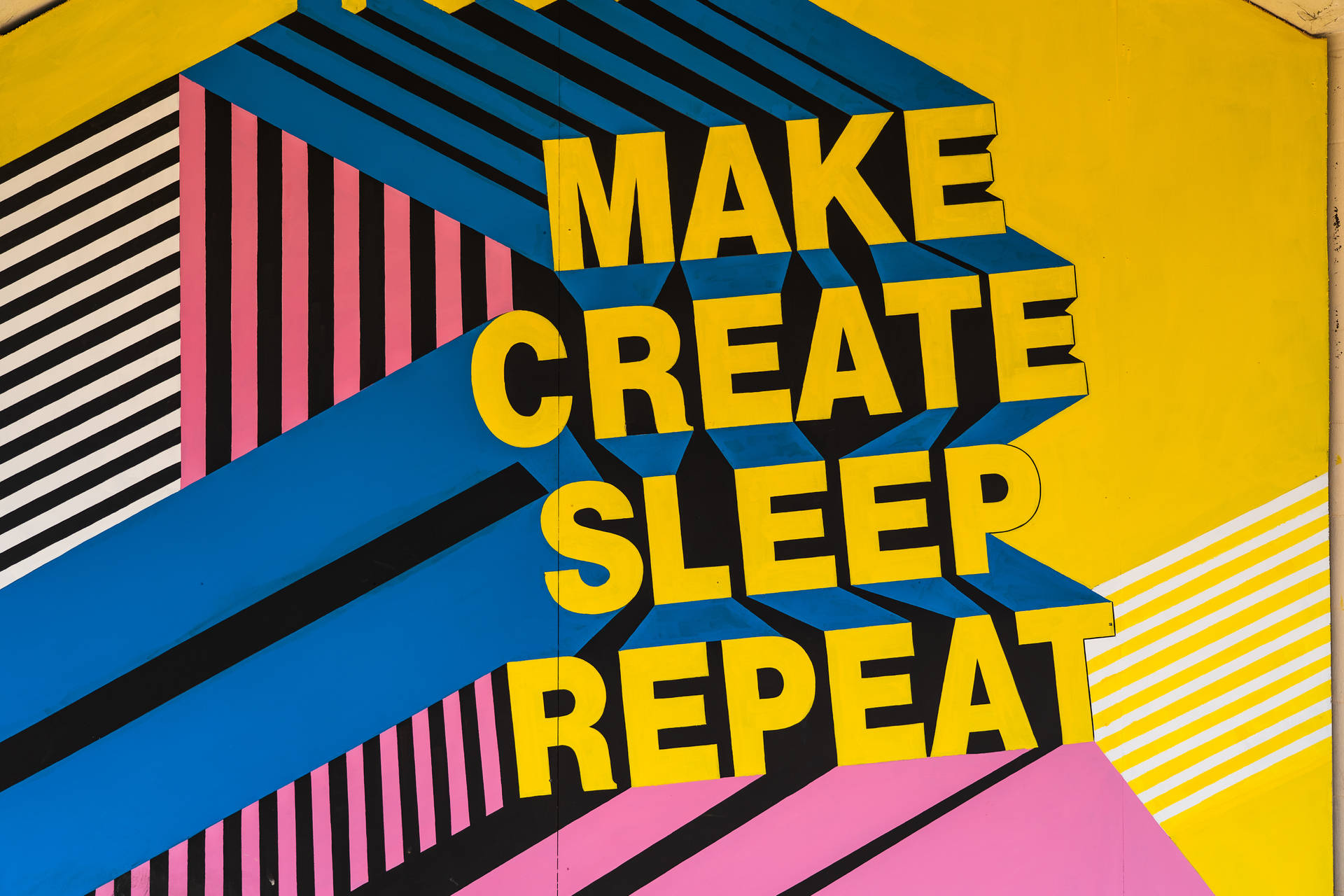 色彩繽紛的幾何壁畫上，粗體黃色文字寫著 make create sleep repeat。