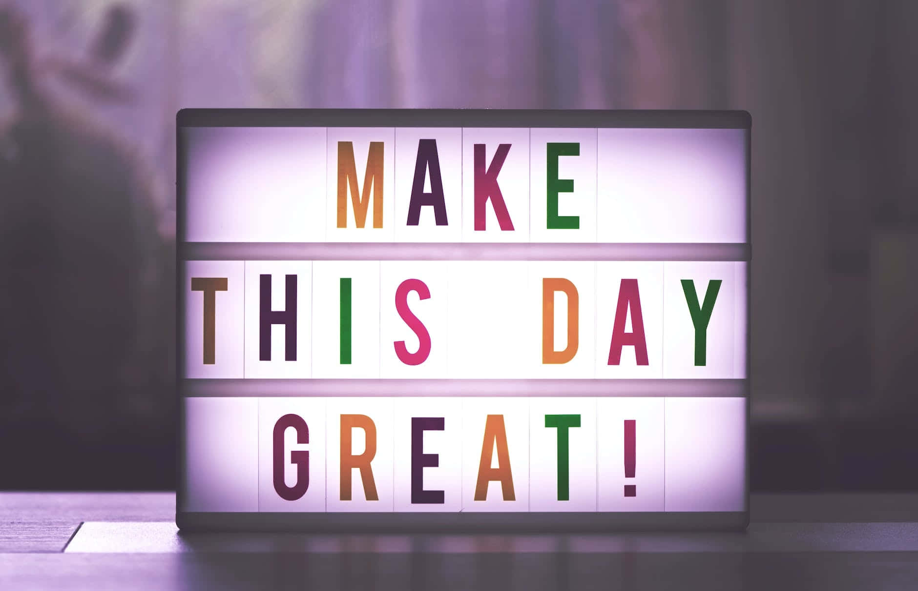  壁紙 — 一個明亮多彩的標誌在柔和模糊的背景上寫著「MAKE THIS DAY GREAT!」。