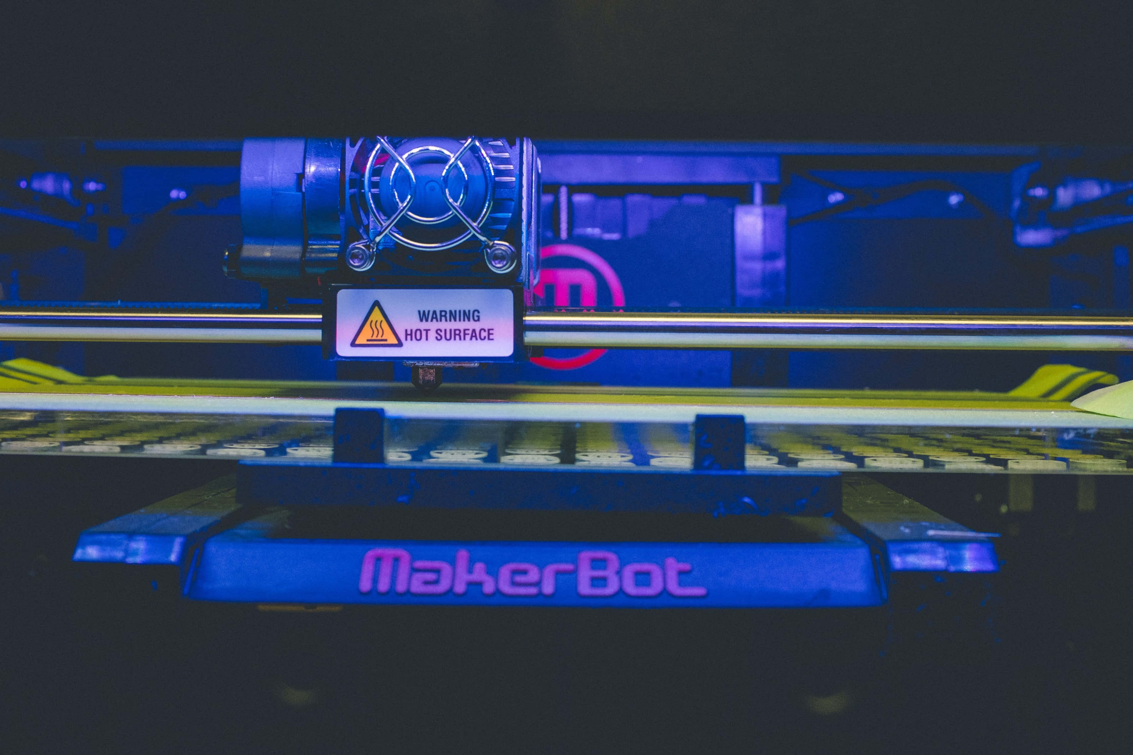 3d Printer 桌布 壁紙 — MakerBot 3D打印機在藍光下發光，其高溫表面帶有警告標籤。