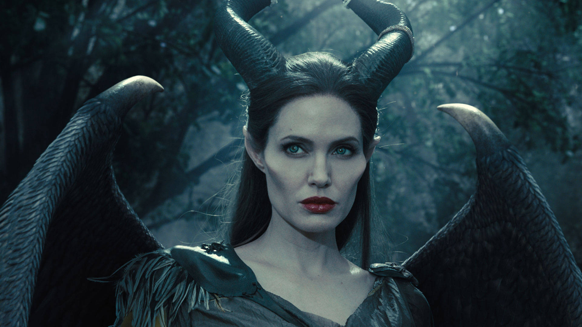 Maleficent 長髮披肩 壁紙 — 一位深色頭髮的女性，擁有發光的綠色眼睛和黑色角，從霧氣瀰漫的森林中凝視，她巨大的黑色翅膀展開。