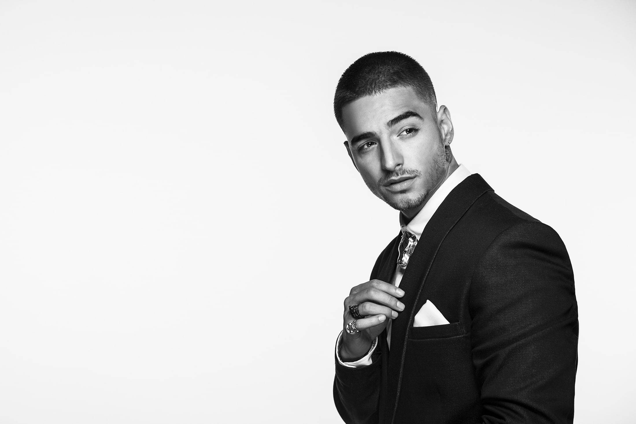 Maluma 黑白西裝造型 壁紙 — 一位穿著黑色西裝、打扮俐落的男士，在純白背景前自信擺姿勢的黑白肖像。