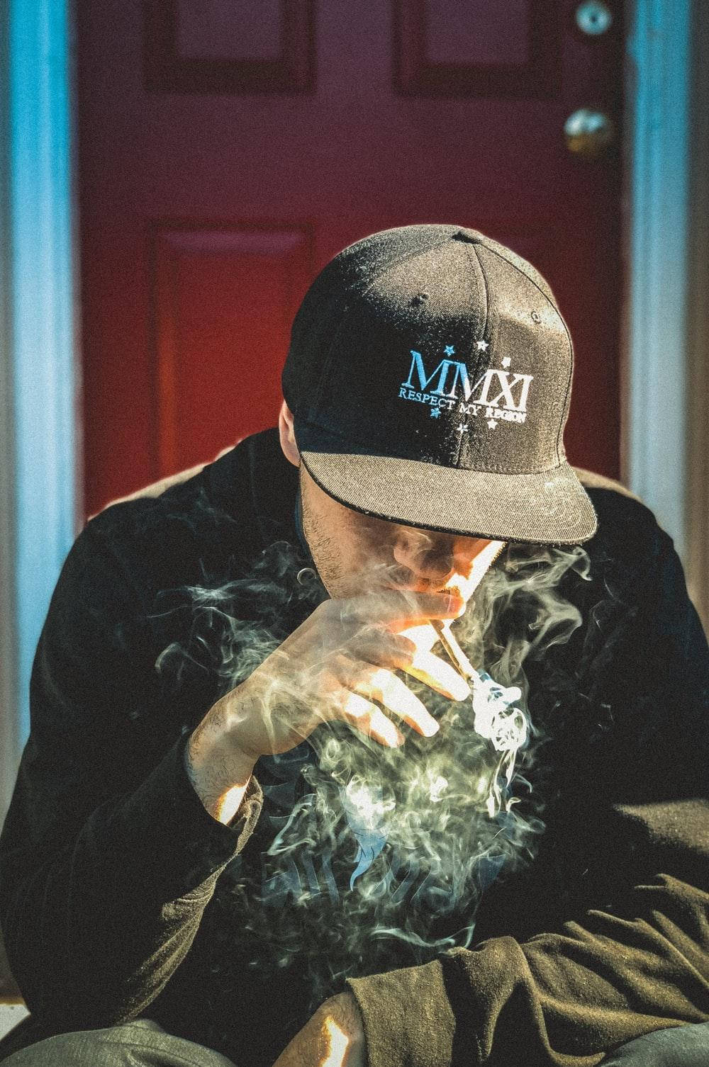 戴鴨舌帽的男人在紅色門前抽煙，煙霧縈繞。