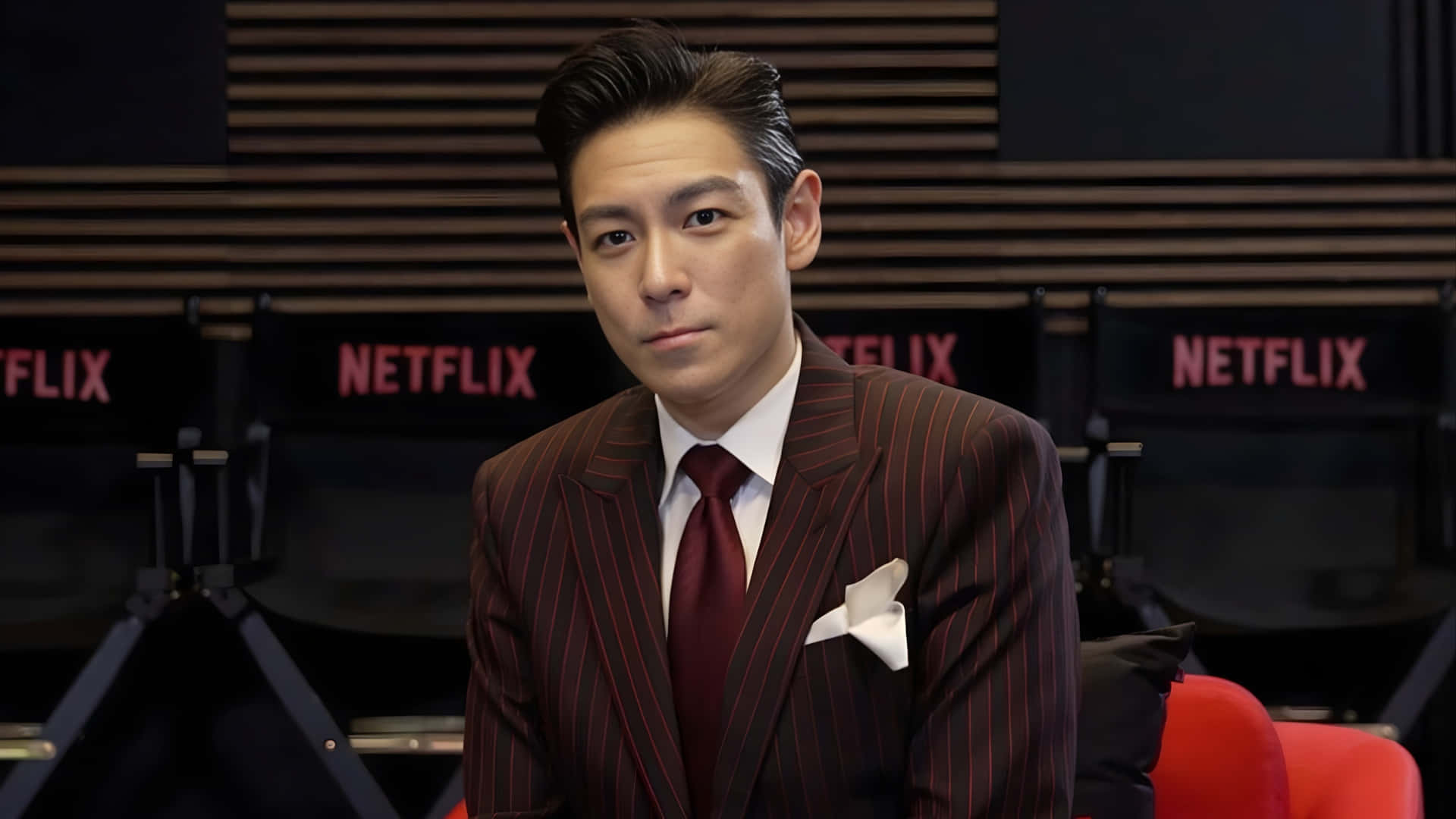 壁紙 — 一名穿著細條紋西裝的男子自信地坐在Netflix品牌椅子前，表情嚴肅。