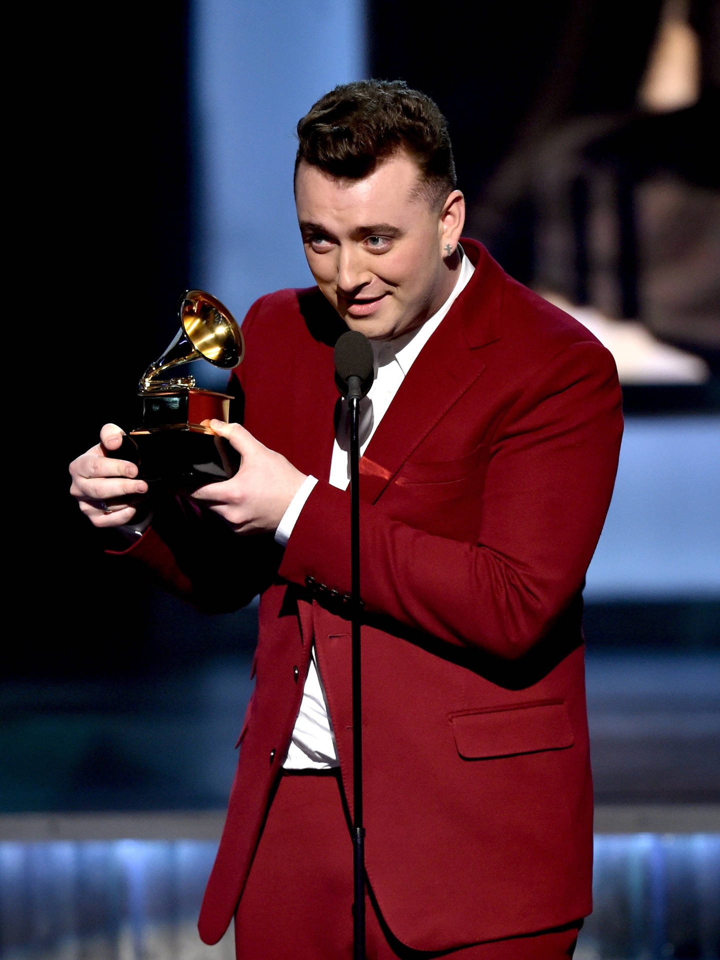 Sam Smith 格萊美獎得主 壁紙 — 一名身穿紅色西裝的男子在燈光昏暗的舞台上手持格林美獎和麥克風。