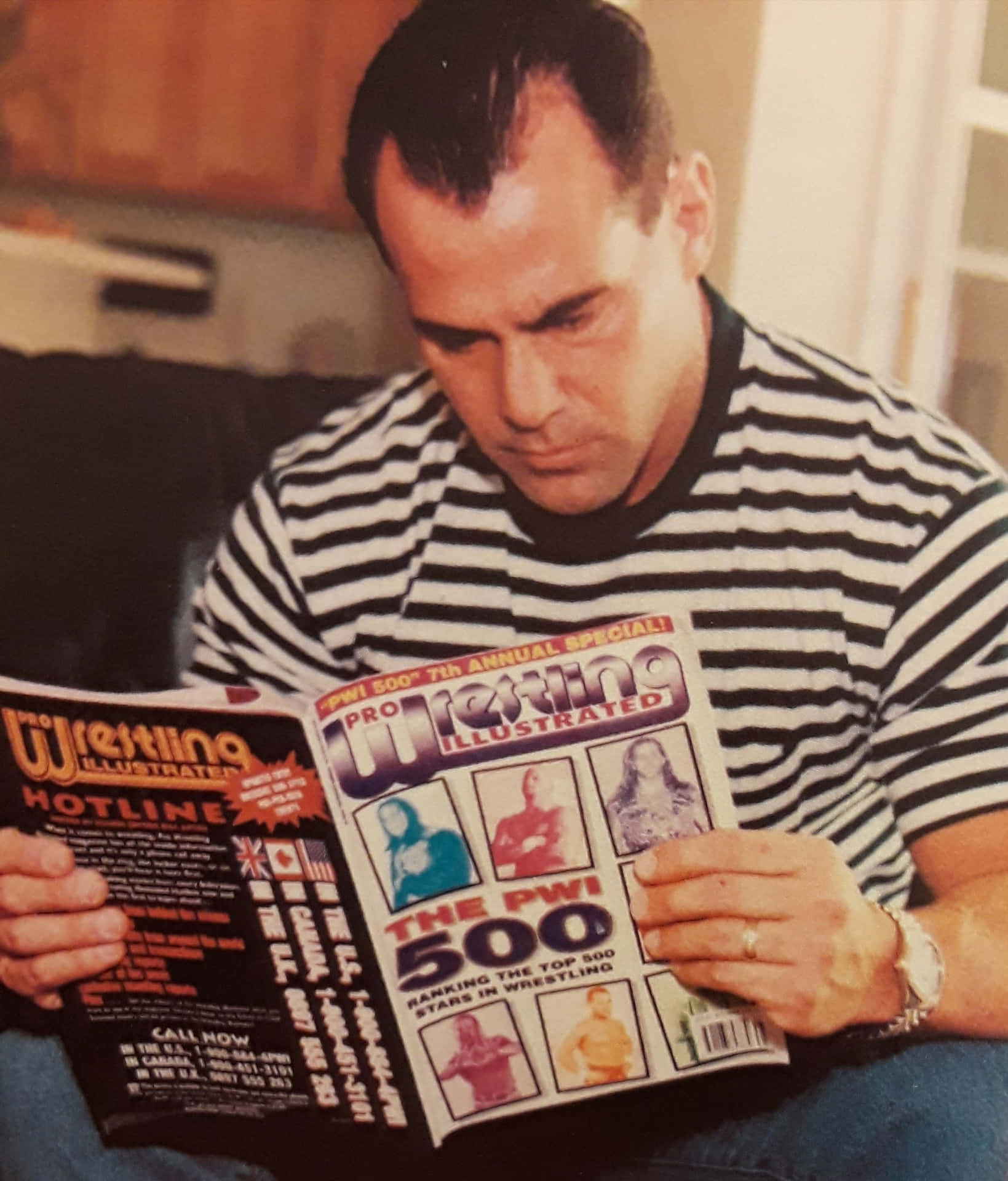  壁紙 — 一名身穿黑白條紋襯衫的男子在室內溫暖燈光下閱讀Pro Wrestling Illustrated雜誌。