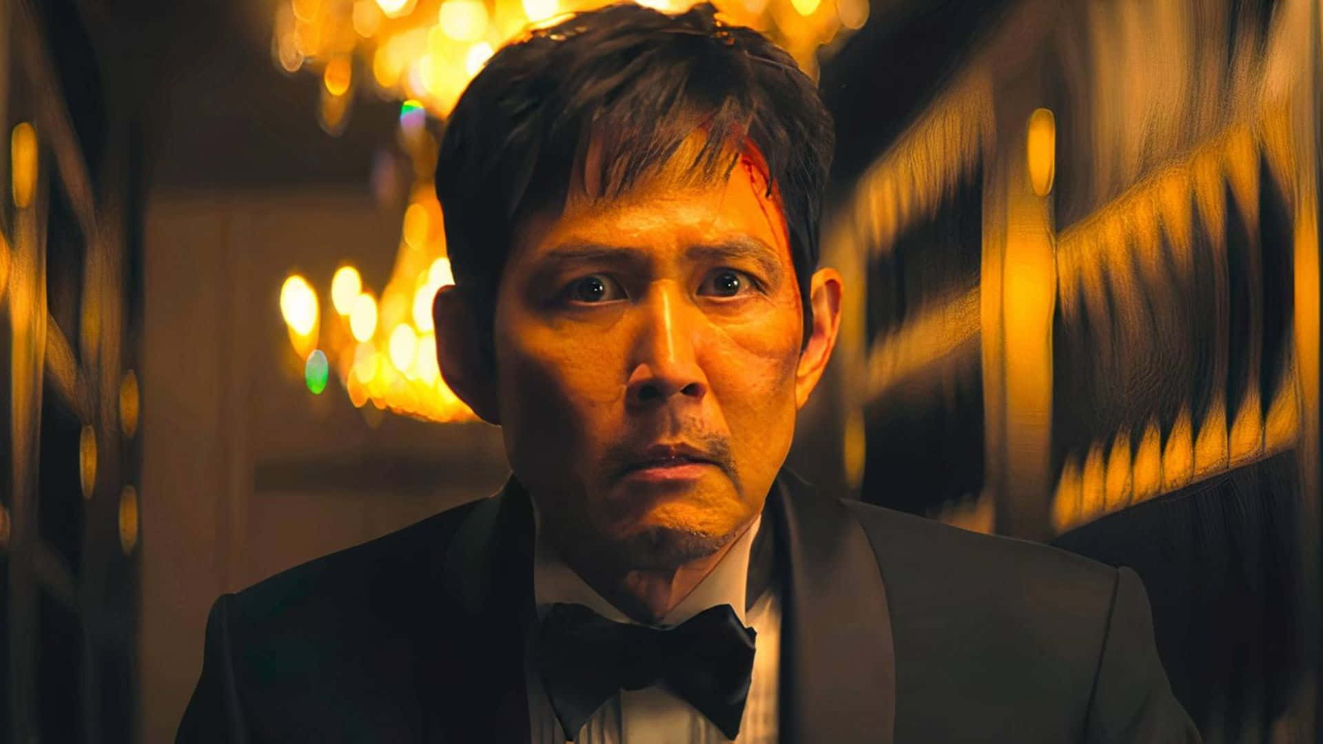  壁紙 — 一名身穿燕尾服、額頭帶血的男子在豪華走廊的溫暖吊燈燈光下凝視著。