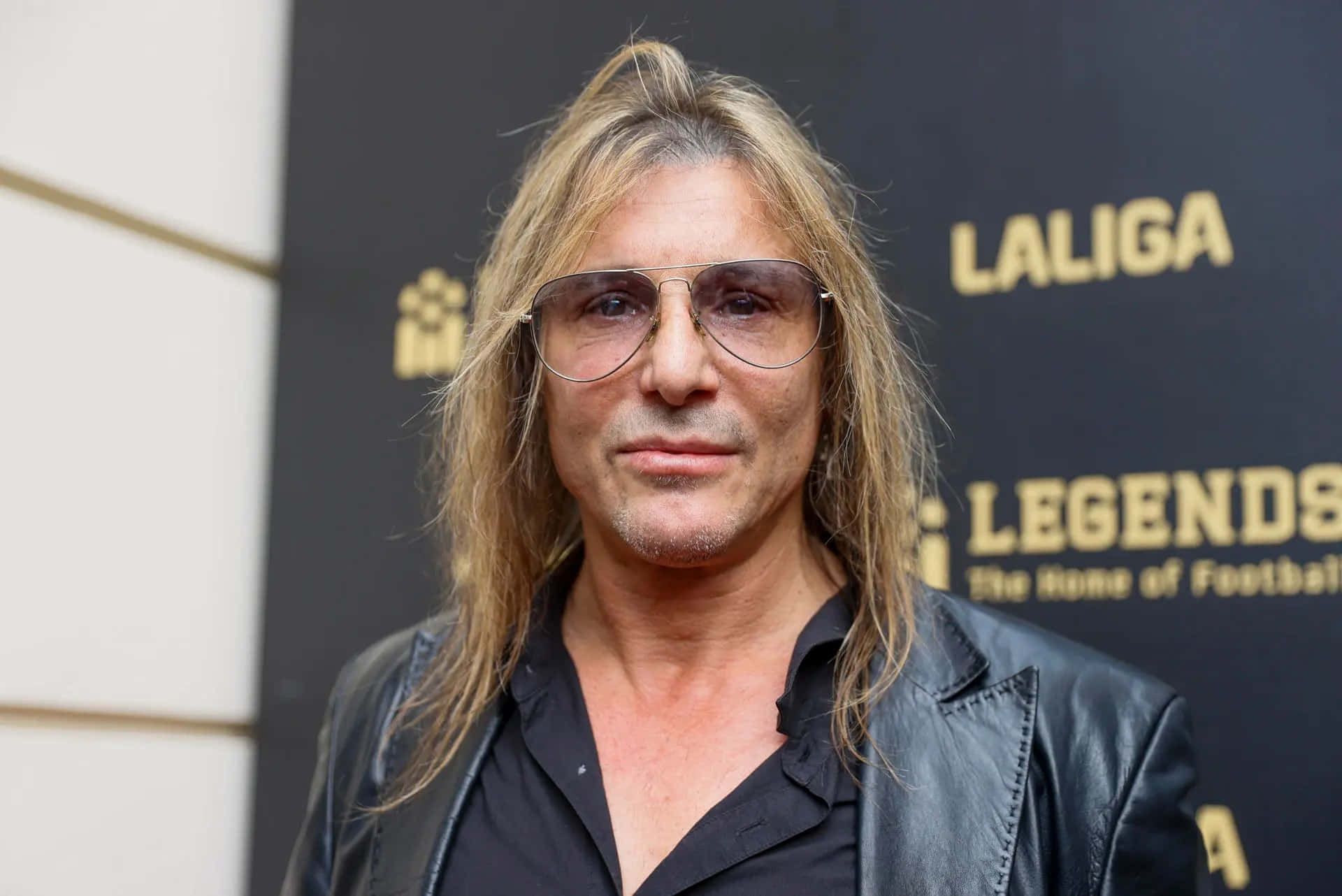  壁紙 — 一位長金髮、戴飛行員太陽眼鏡的男子，身穿黑色皮褸在Laliga Legends活動中擺姿勢。