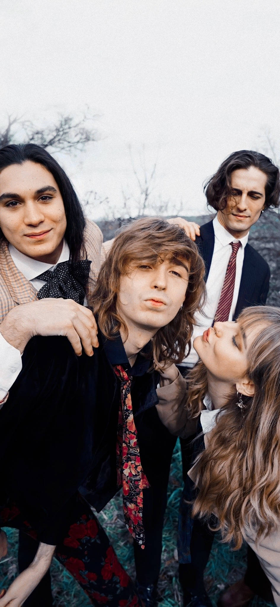 Maneskin 輕鬆即興攝影 壁紙 — 四位時尚年輕人在陰沉多雲的戶外環境中緊密擺姿勢，背後有光禿的樹木。