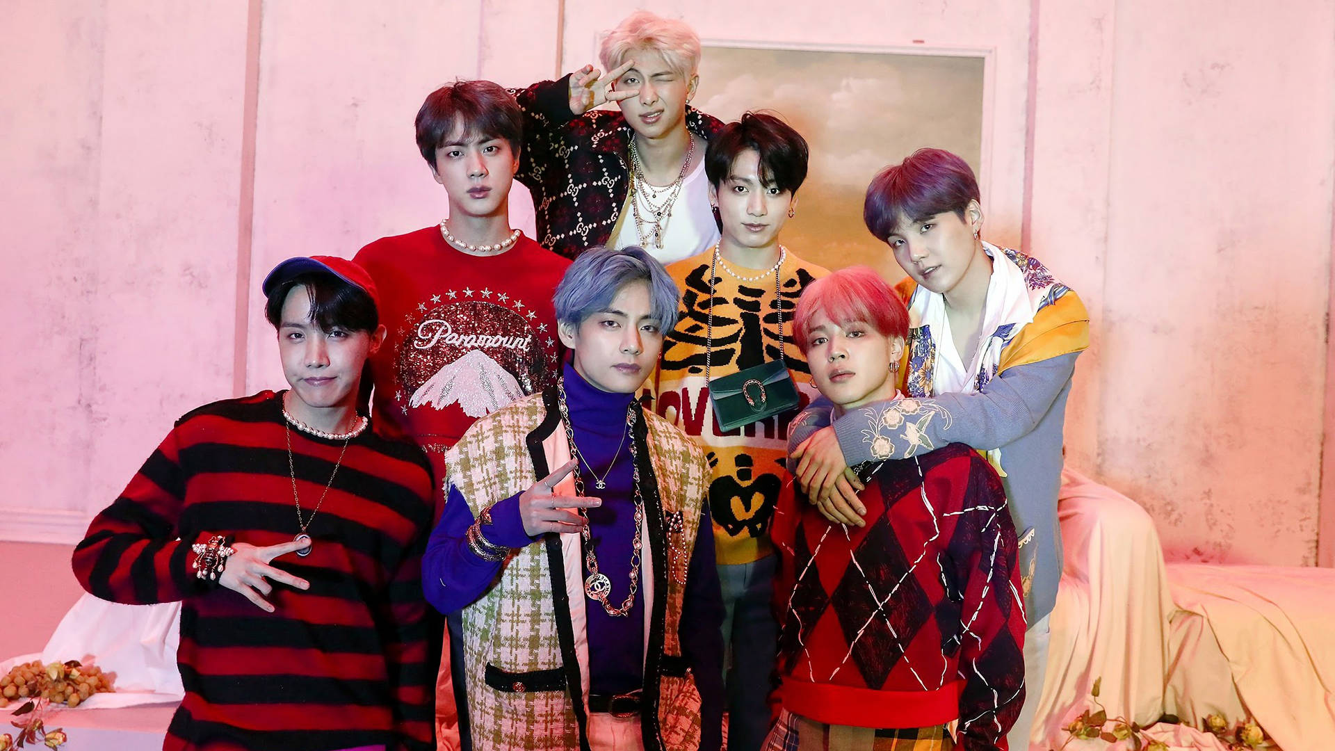《Map of the Soul: Persona》粉嫩背景BTS筆電壁紙 壁紙 — 七位時尚年輕男士身穿色彩繽紛的圖案服裝，在帶有花卉裝飾的柔軟粉紅色紋理牆前自信地擺姿勢。