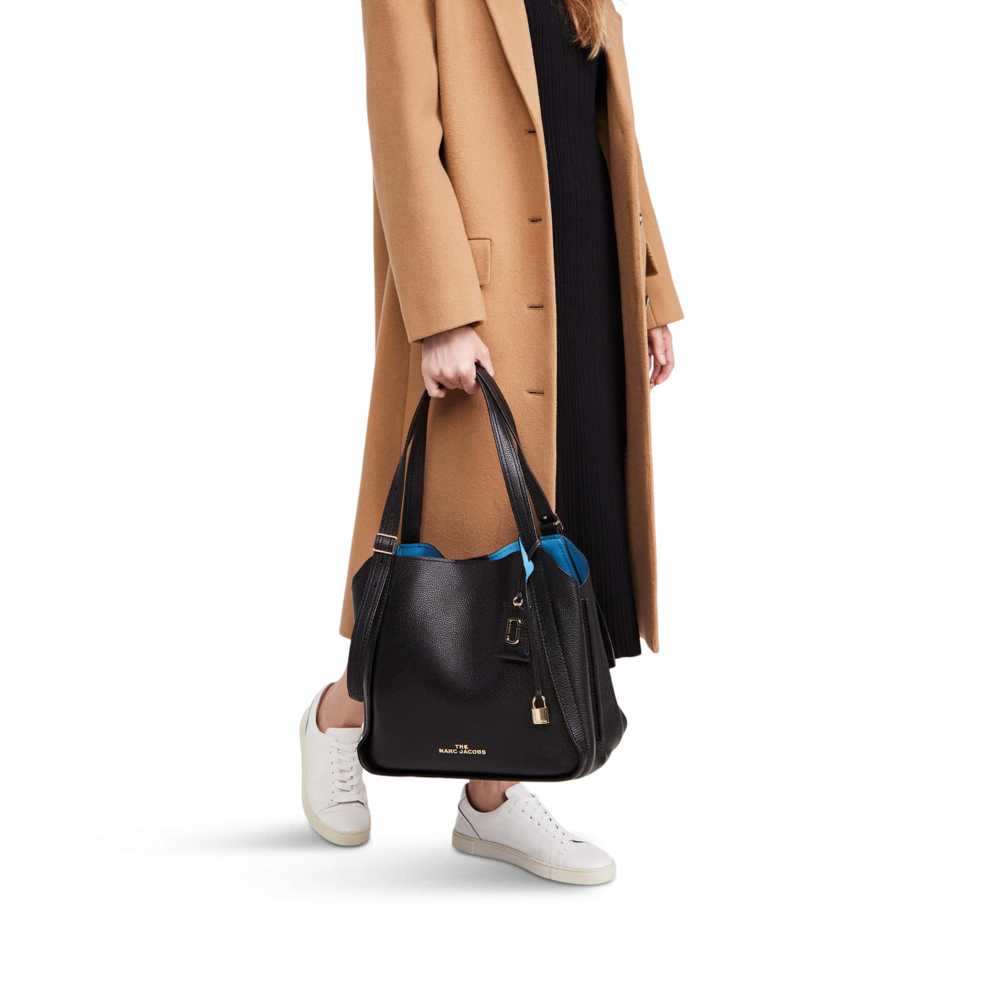 身穿駝色大衣和白色運動鞋的女性，拿著帶有藍色內襯的黑色手提包。