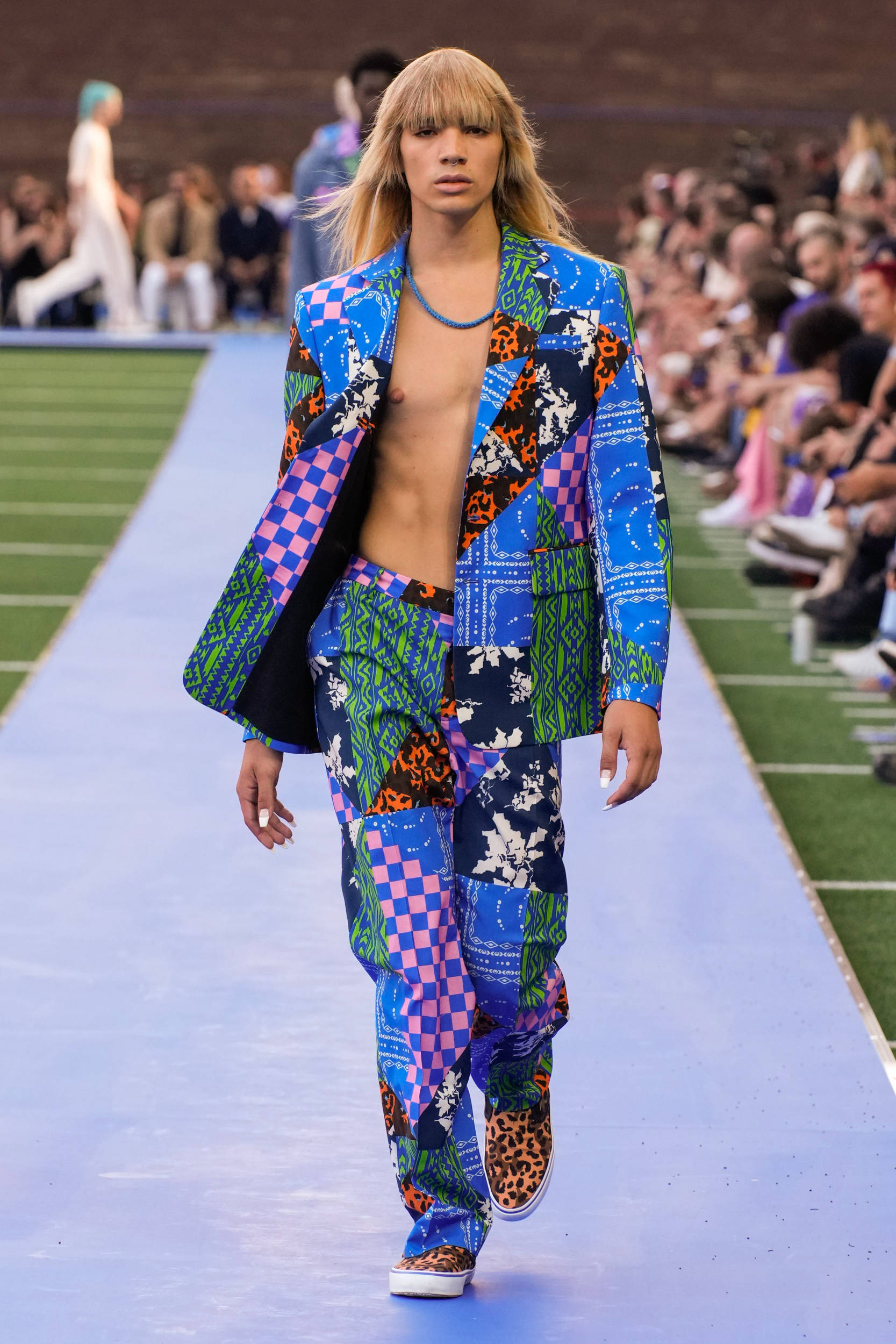 Marcelo Burlon 獨特美學印花高質T恤 壁紙 — 一名模特兒在藍色天橋上走秀，身穿色彩鮮豔的拼布套裝，帶有豹紋和幾何圖案。