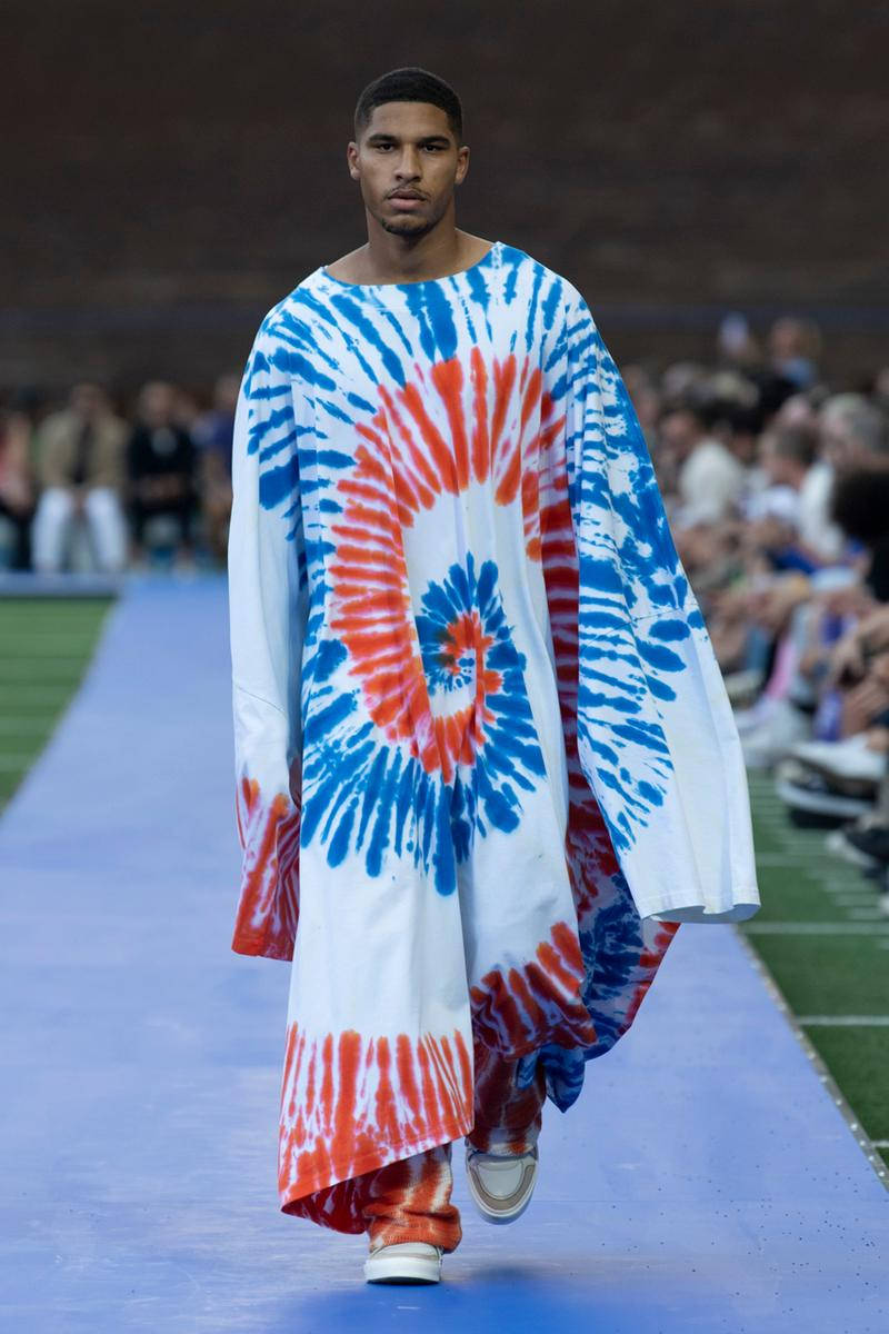 Marcelo Burlon 街頭風格：掌握叛逆時尚藝術 壁紙 — 模特兒自信地走在藍色天橋上，身穿搶眼的紅、藍、白紮染長袍，在明亮燈光下。