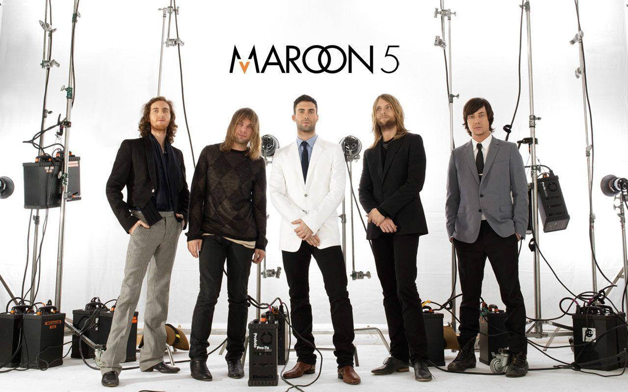 Maroon 5 舞台樂器多雲天空 壁紙 — Maroon 5 樂隊成員在一個可見照明設備和他們標誌的錄音室中自信地擺姿勢。