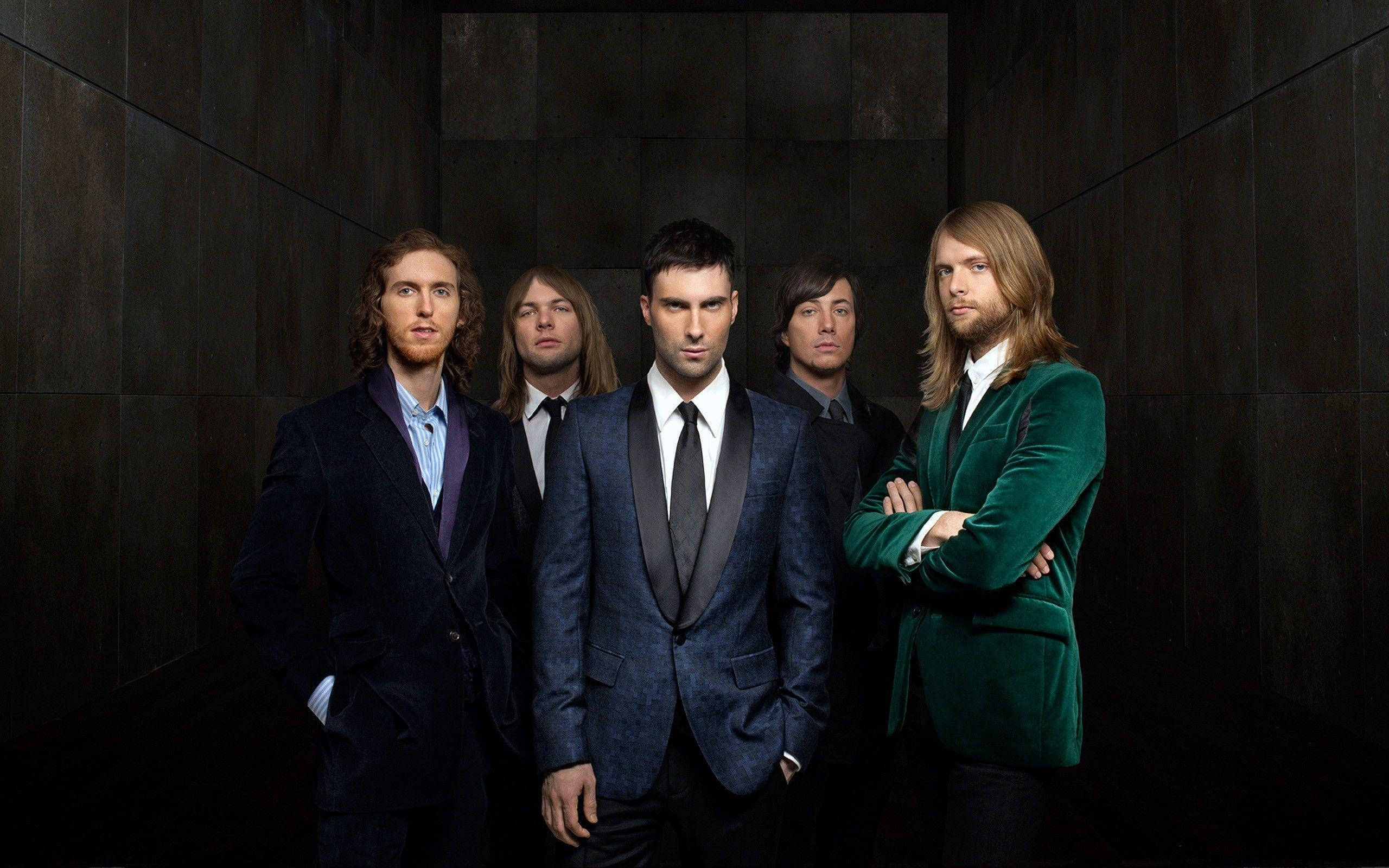 Maroon 5 西裝黑底壁紙 壁紙 — 五位身穿時尚西裝的男士在陰暗的紋理牆壁前自信地擺姿勢，營造出充滿氛圍的工作室肖像。