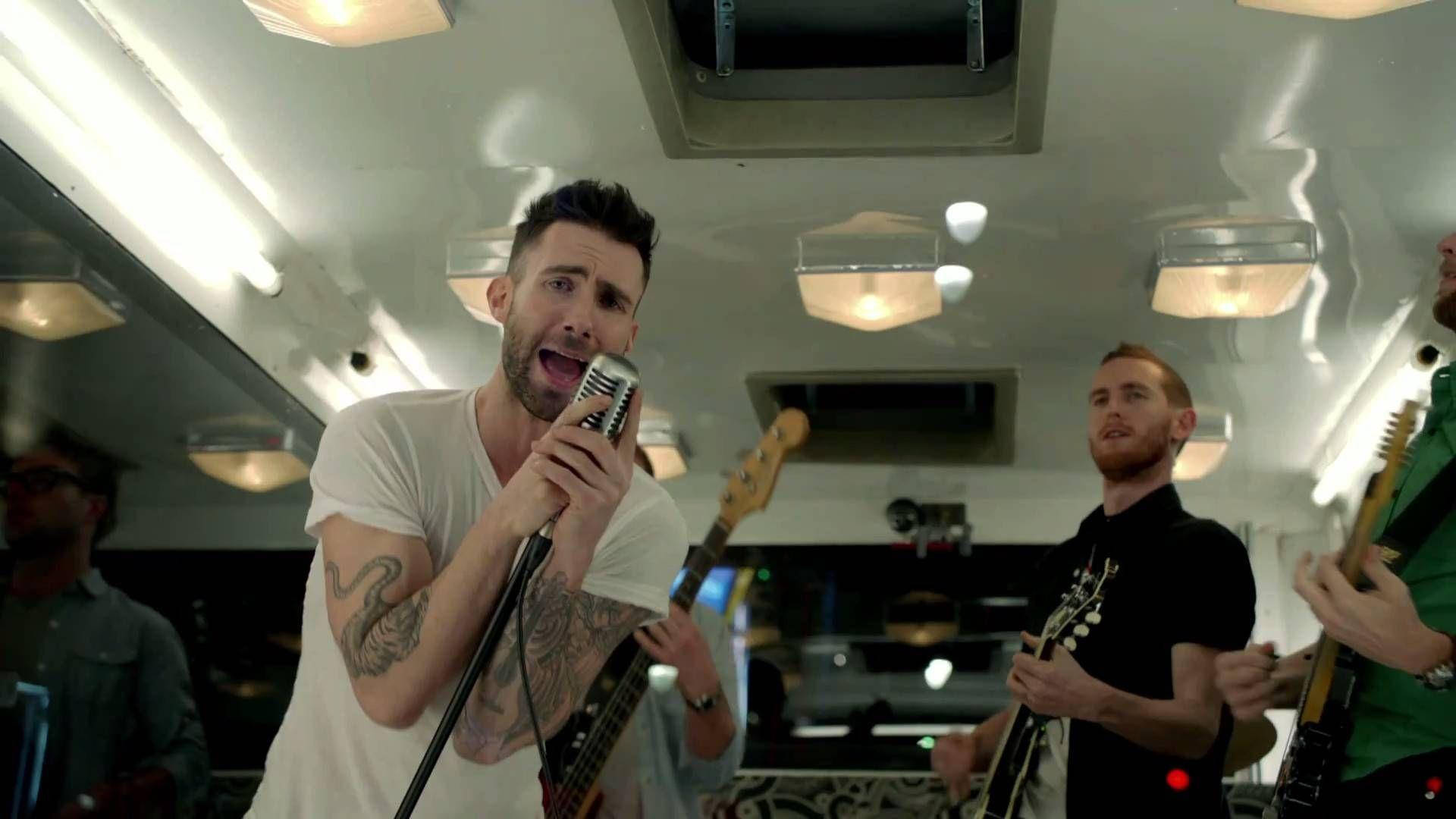 Maroon 5 亞當·列文 白色T恤演唱 壁紙 — 樂隊在復古飛機內充滿活力地表演，主唱手持麥克風，結他手在溫暖的頂燈下演奏。