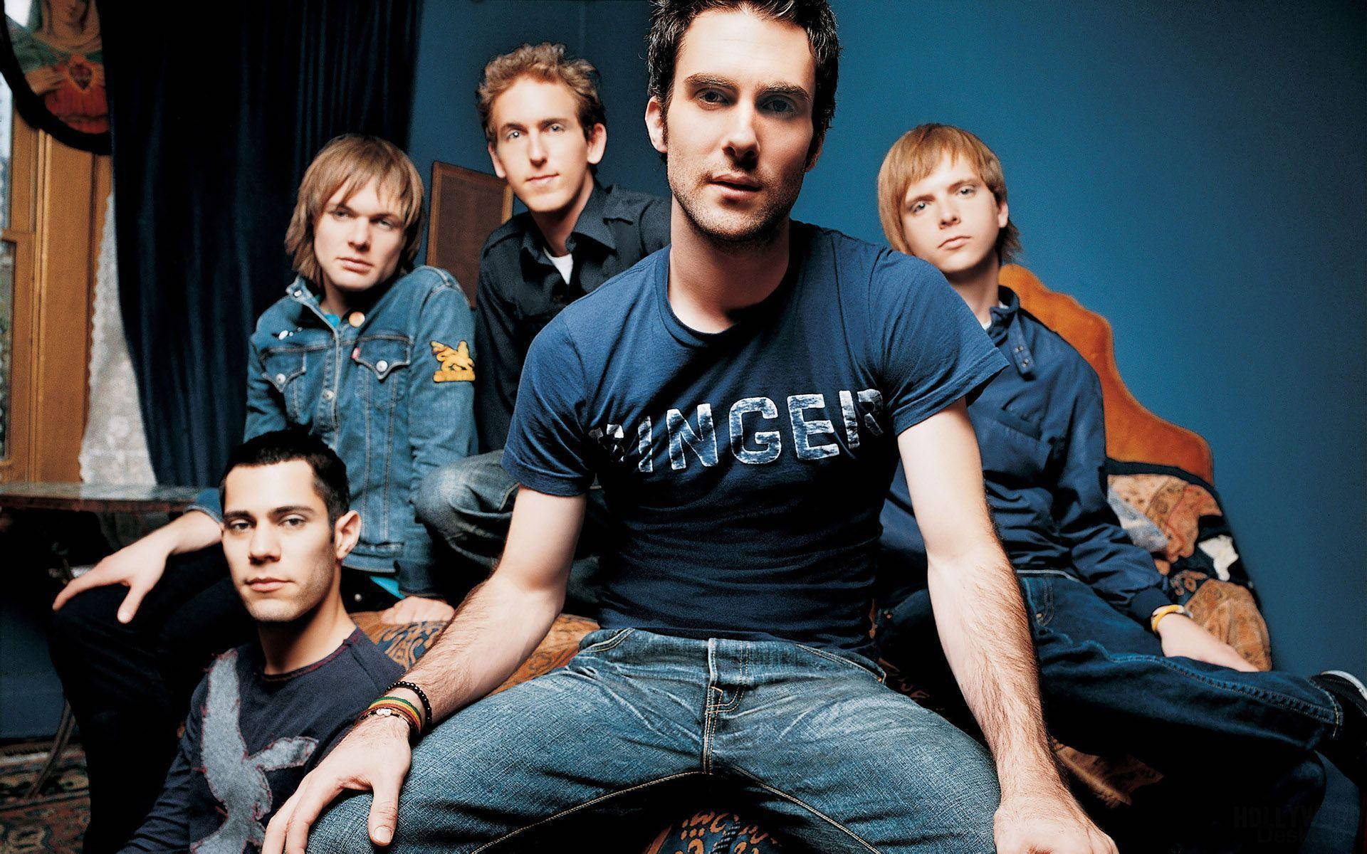Maroon 5 帶隊成員藍色服裝藍色房間 壁紙 — 五位年輕男士身穿休閒牛仔褲和T恤，在深藍色牆壁前的圖案沙發上自信地擺姿勢。