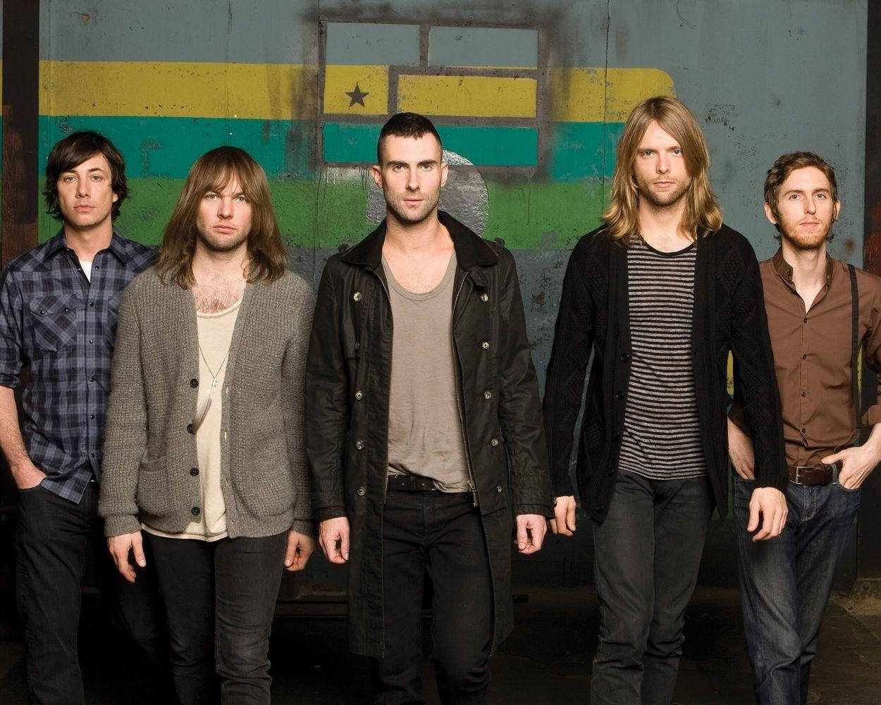 Maroon 5 成員穿著嘻哈風外套 壁紙 — 五位身穿休閒服裝的男子自信地站在一面風化的牆前，牆上有褪色的黃、綠、藍條紋和一顆星星。