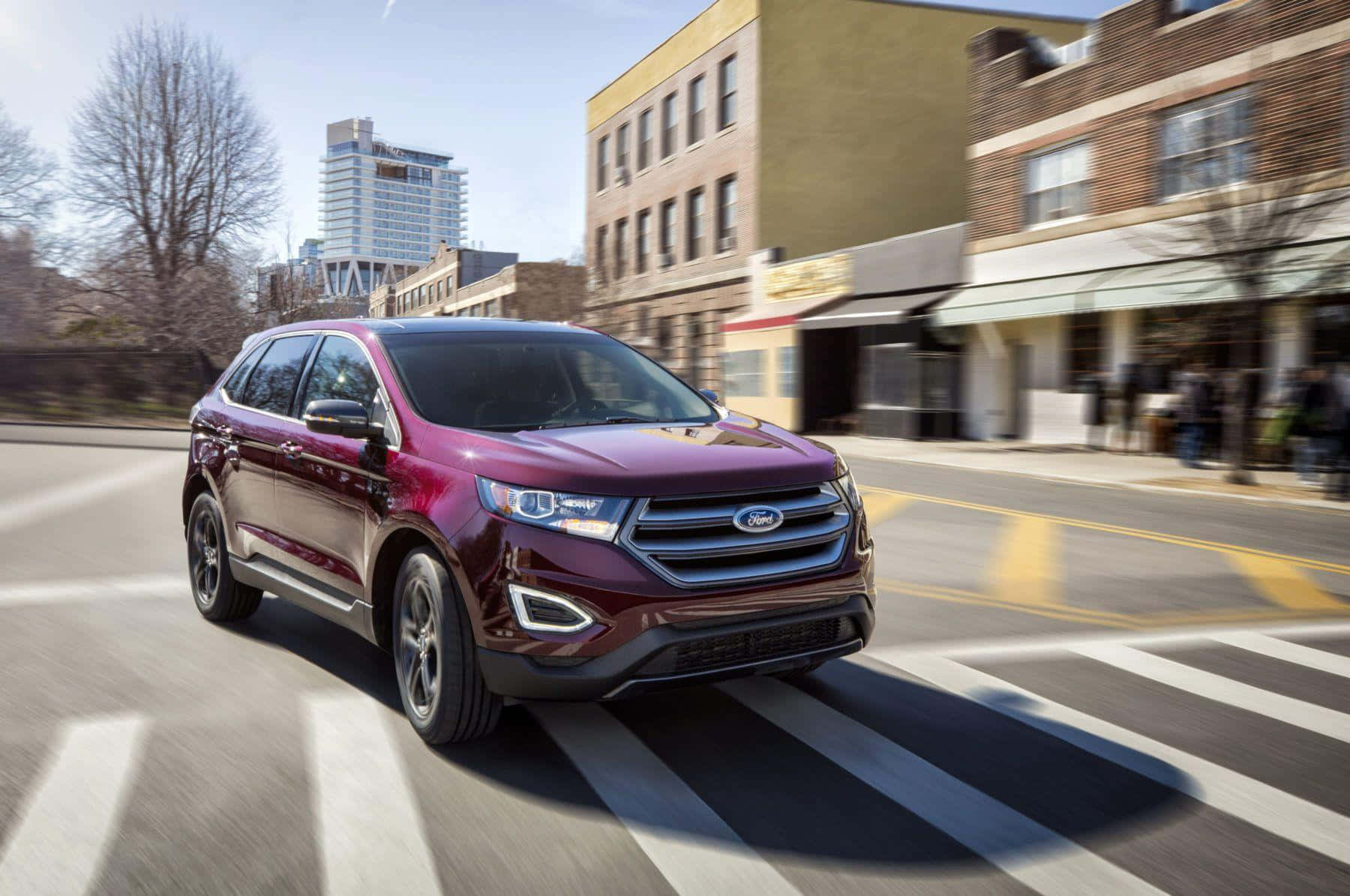 Ford Edge 桌布 壁紙 — 一輛栗色福特Edge SUV在陽光明媚的城市街道上疾馳，建築物和斑馬線條紋模糊不清。