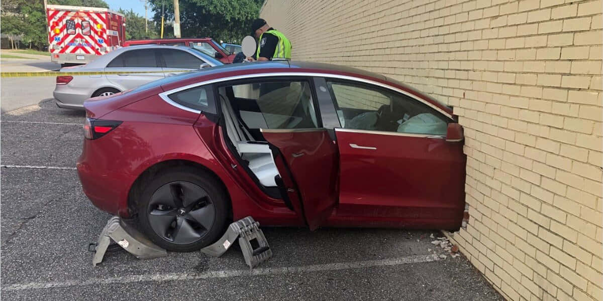 Tesla Model Y 桌布 壁紙 — 一輛栗色Tesla房車撞向米色磚牆，車門打開，應急人員在附近。