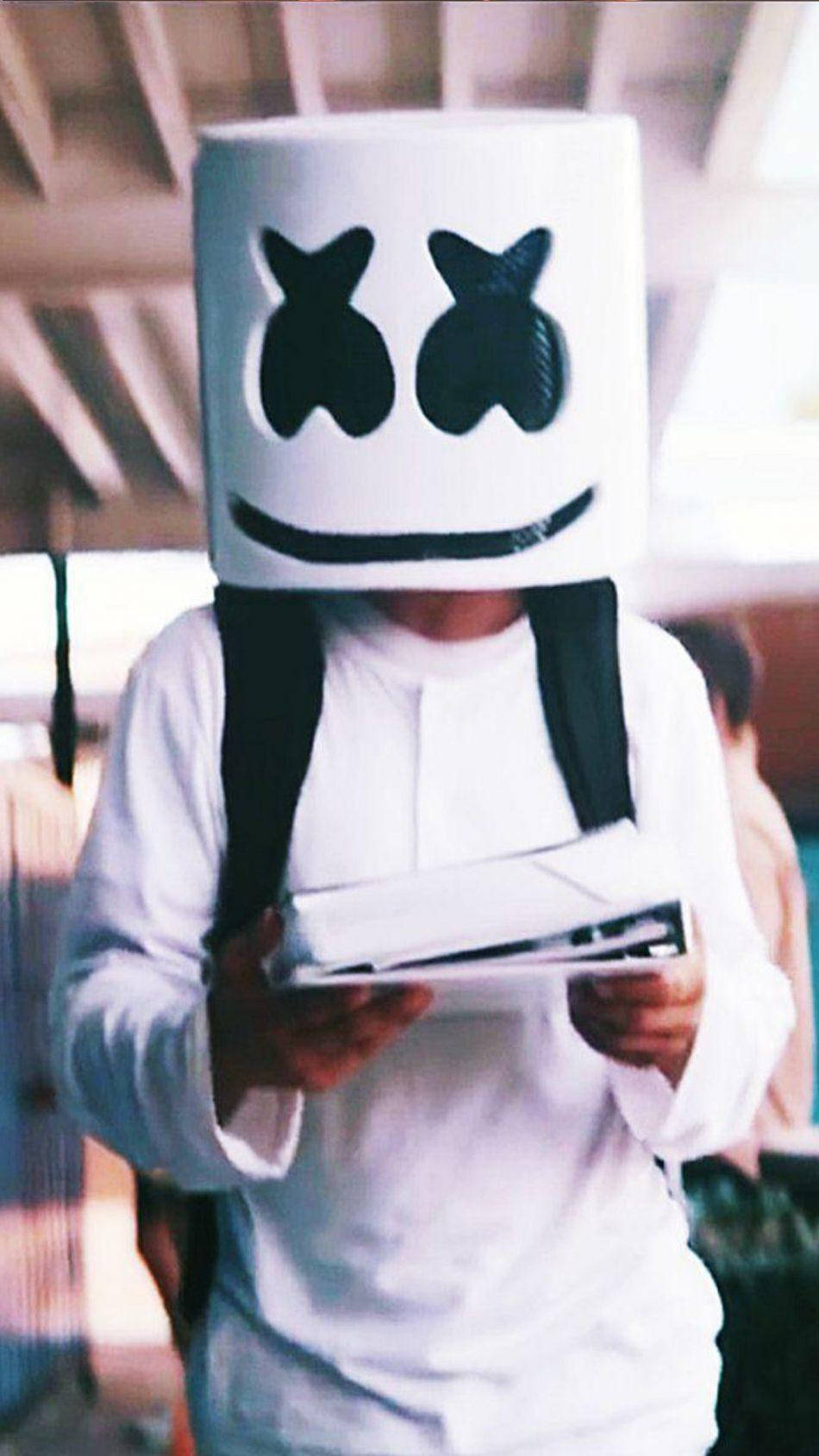 Marshmello iPhone 手持書籍 壁紙 — 一個穿著白色棉花糖頭盔服裝的人，在柔和的室內燈光下拿著一本書。