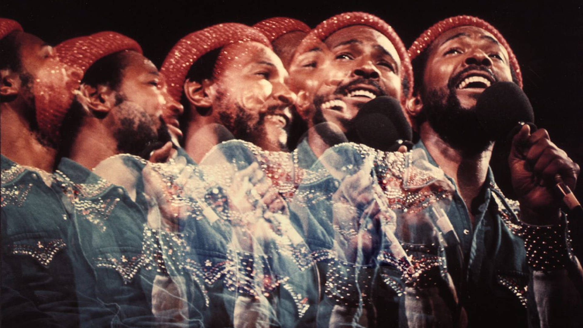 Marvin Gaye 多重演唱會影像 壁紙 — 五個戴紅帽、穿鑲寶石藍色外套的男人在舞台燈光下熱情地對著咪高峰唱歌。