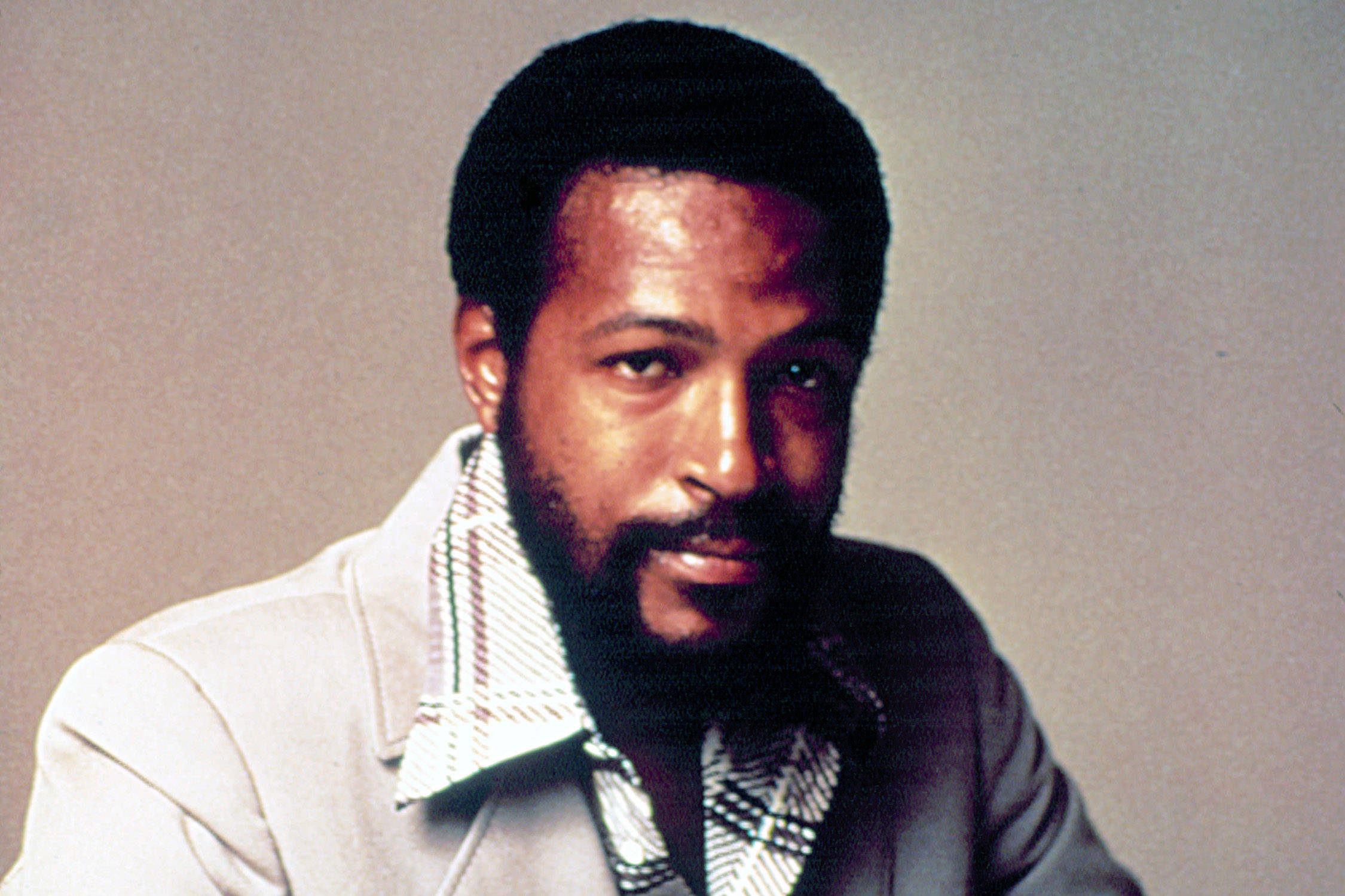Marvin Gaye 穿白服裝 壁紙 — 一位留鬍鬚、短髮的男子，在純色工作室背景前，穿著輕便外套配襯圖案襯衫。