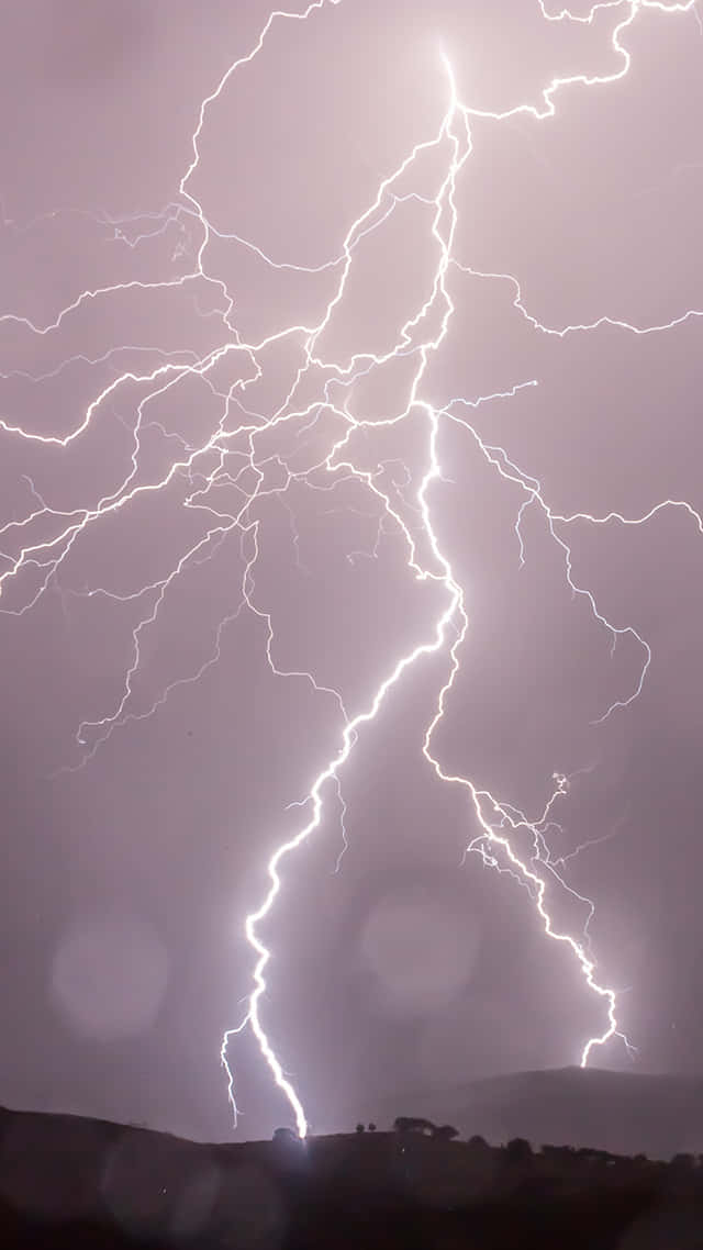 Lightning iPhone 桌布 壁紙 — 一道巨大的閃電在風暴般的紫色天空中分叉，下方是黑暗的剪影山丘。