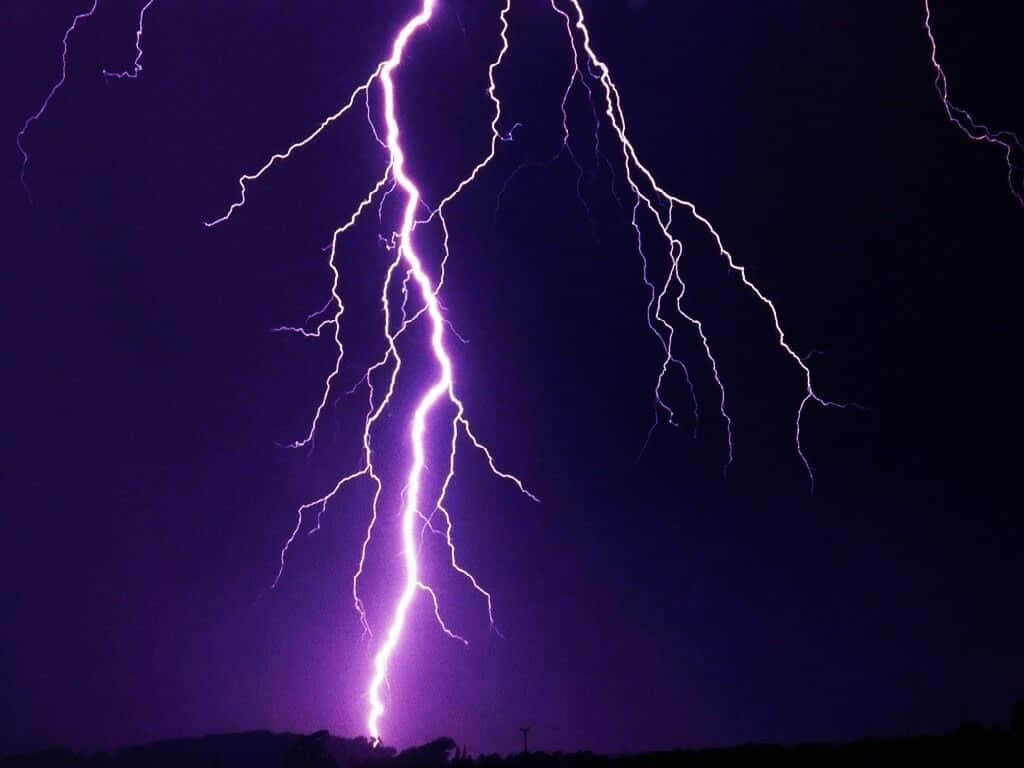 紫色閃電照亮了遠方剪影上方的黑暗夜空。
