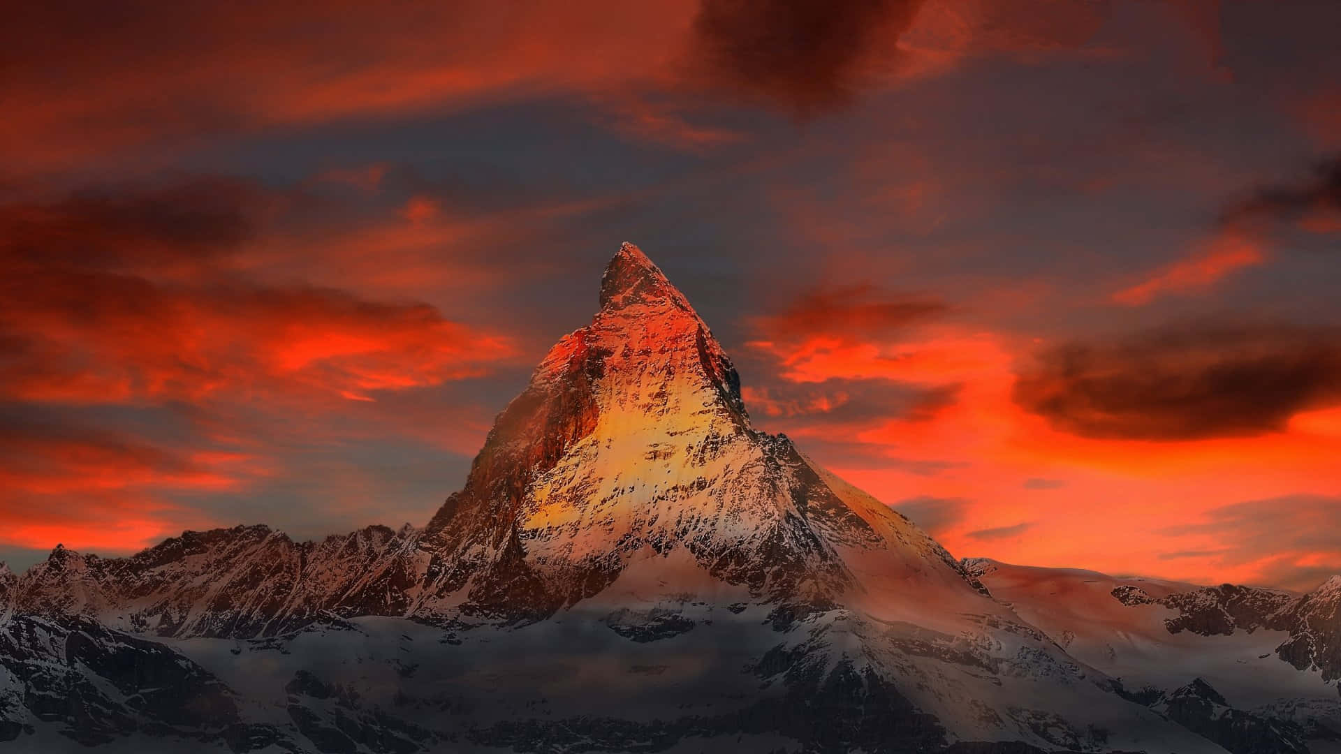 Matterhorn 山峰上的紅色夕陽 壁紙 — 白雪覆蓋的山峰在火紅橙紅色的日落天空和戲劇性的雲彩下閃耀著金色光芒。