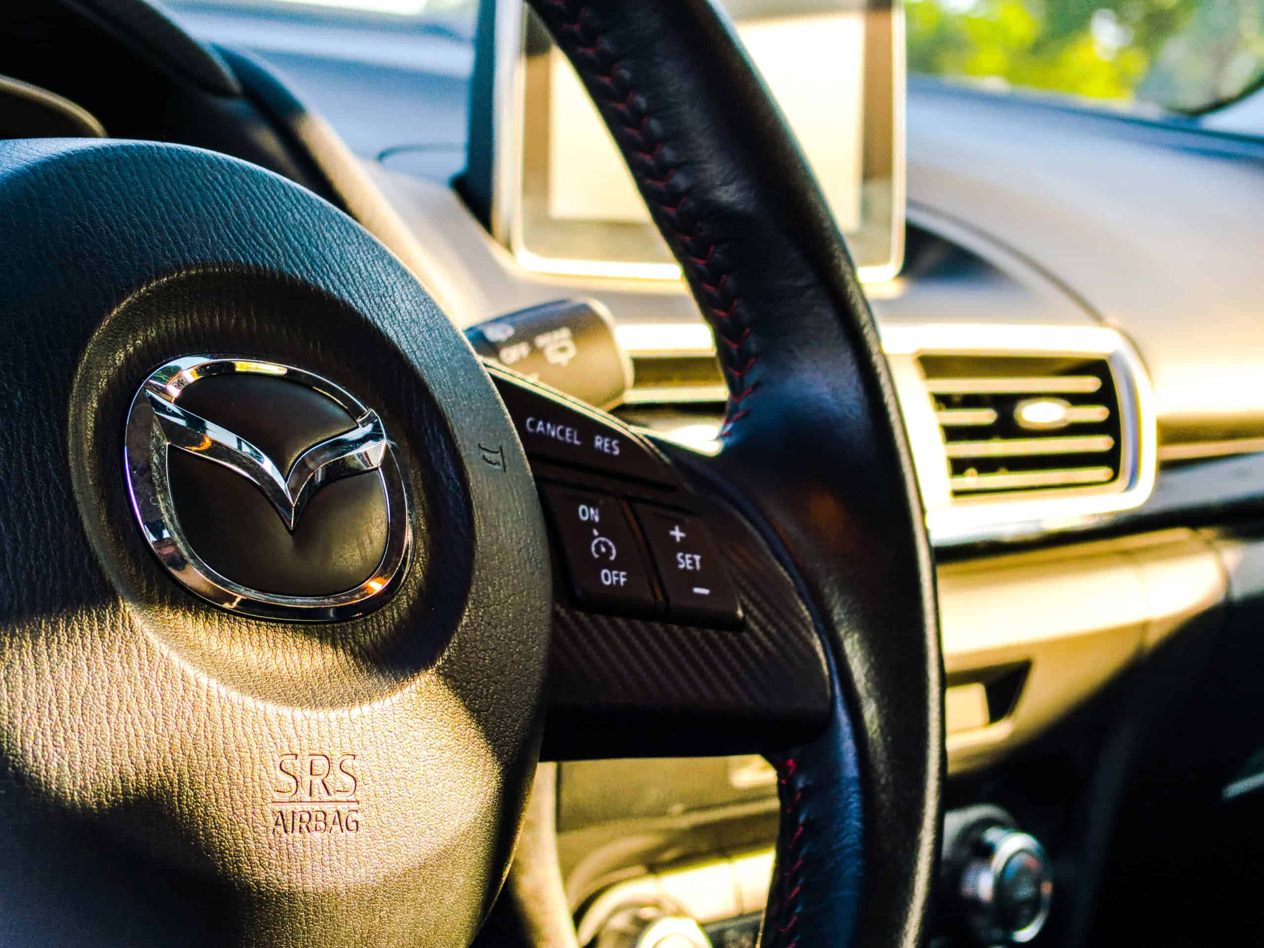 Car Technology 桌布 壁紙 — Mazda 軚盤特寫，紅色縫線及鍍鉻徽章沐浴在溫暖陽光下。
