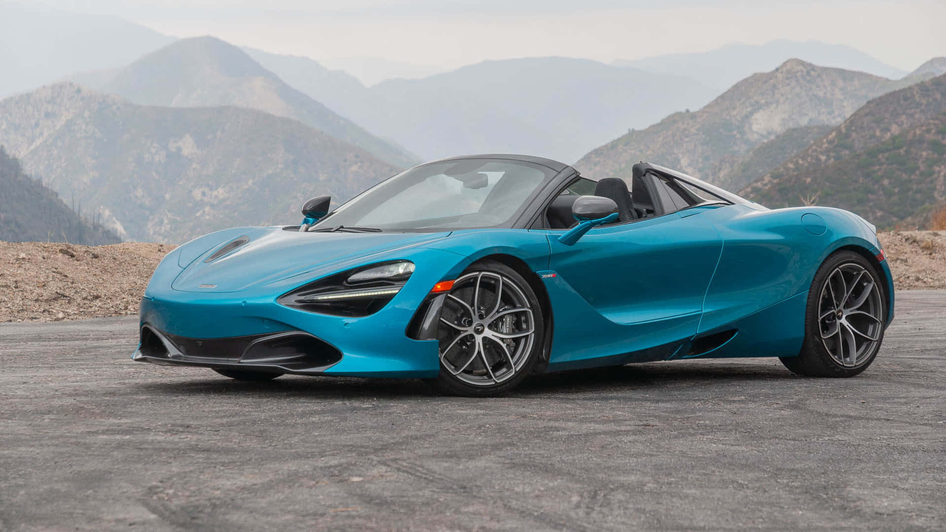 觀景台最佳 McLaren 720S 壁紙 — 一輛充滿活力的藍色McLaren 720S Spider跑車停泊在山路上，背景是崎嶇的山峰。